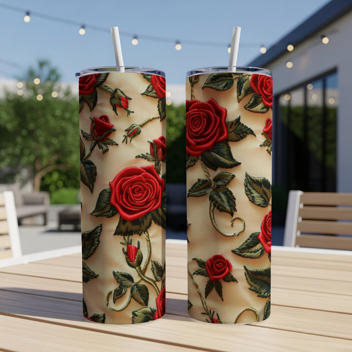 Two tall tumblers with red rose embroidery pattern on a blurred outdoor patio background.