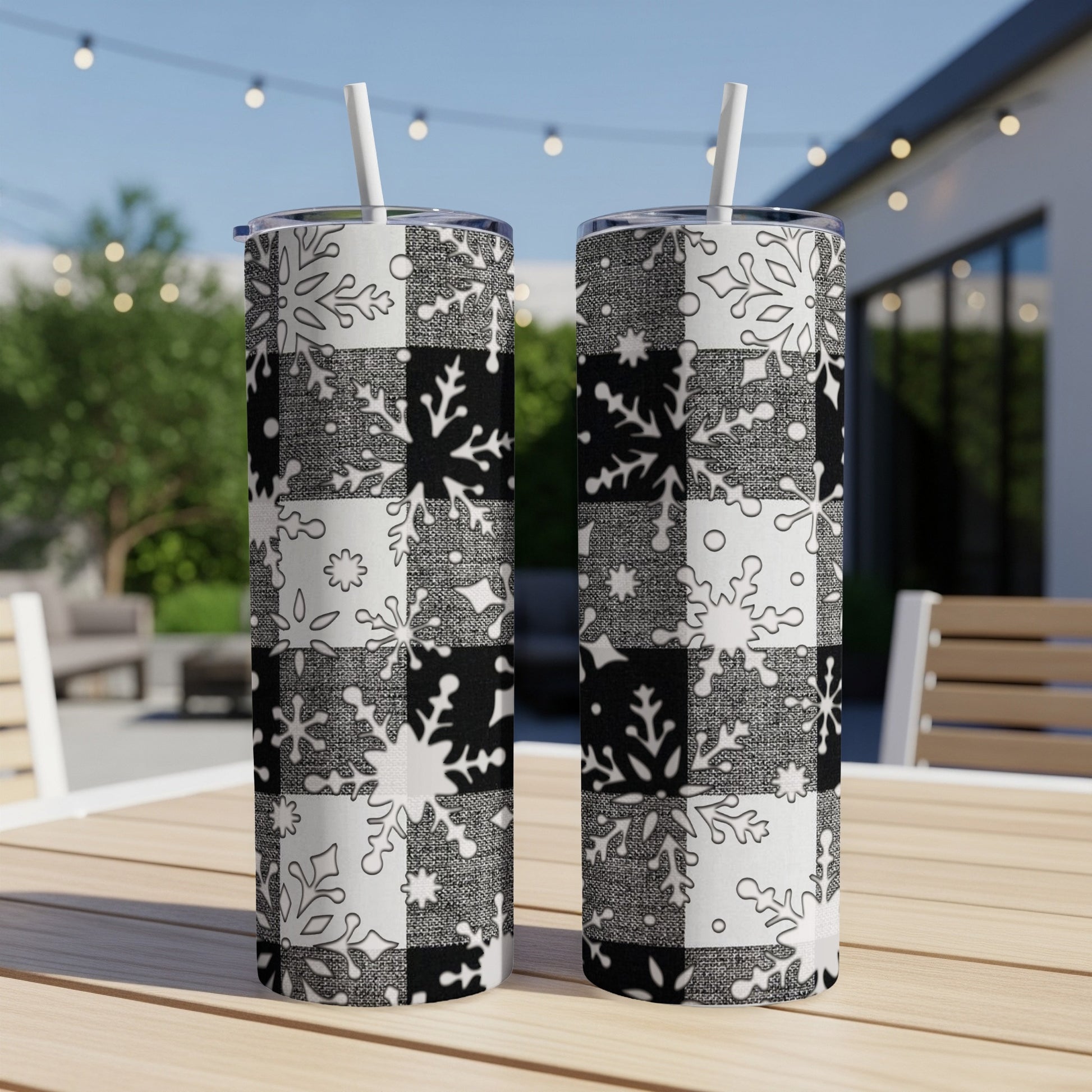 Two black and white snowflake patterned tumblers on a table outdoors.