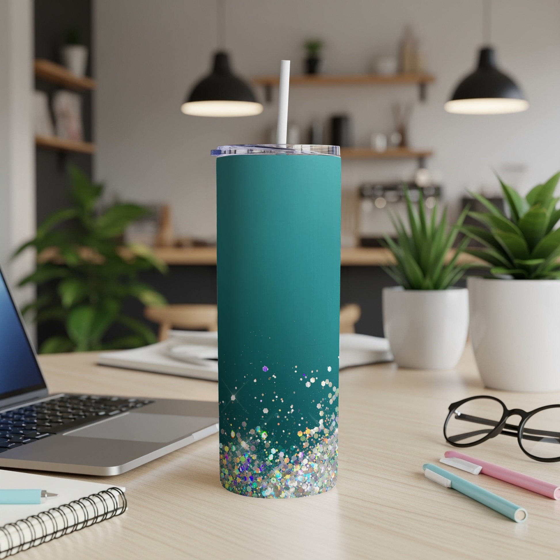 Teal tumbler with glittery bottom and white straw sits on a desk.