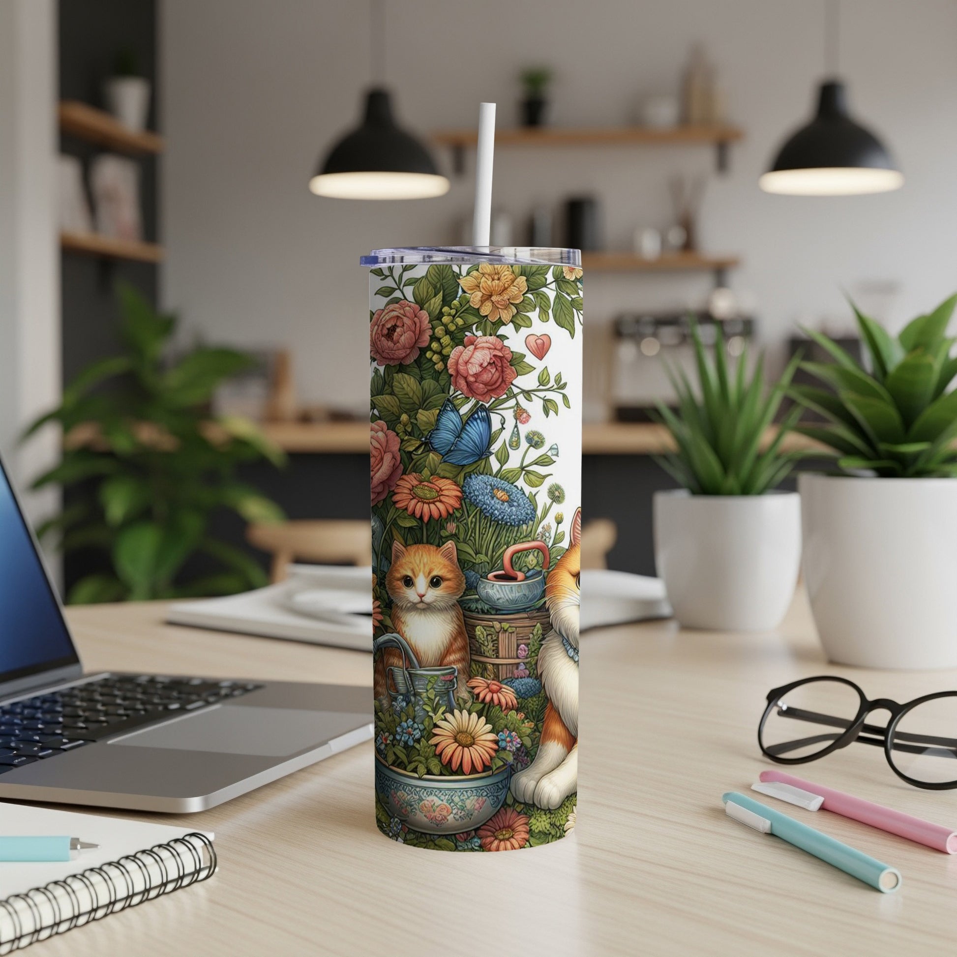 Floral tumbler with cats and butterflies on a desk.