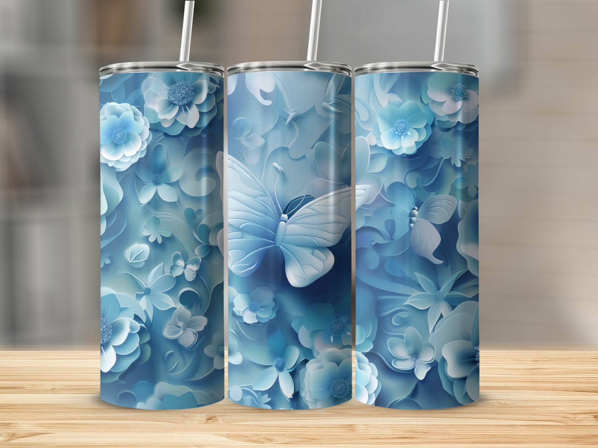Three blue tumblers with butterfly and floral designs on a wooden surface.