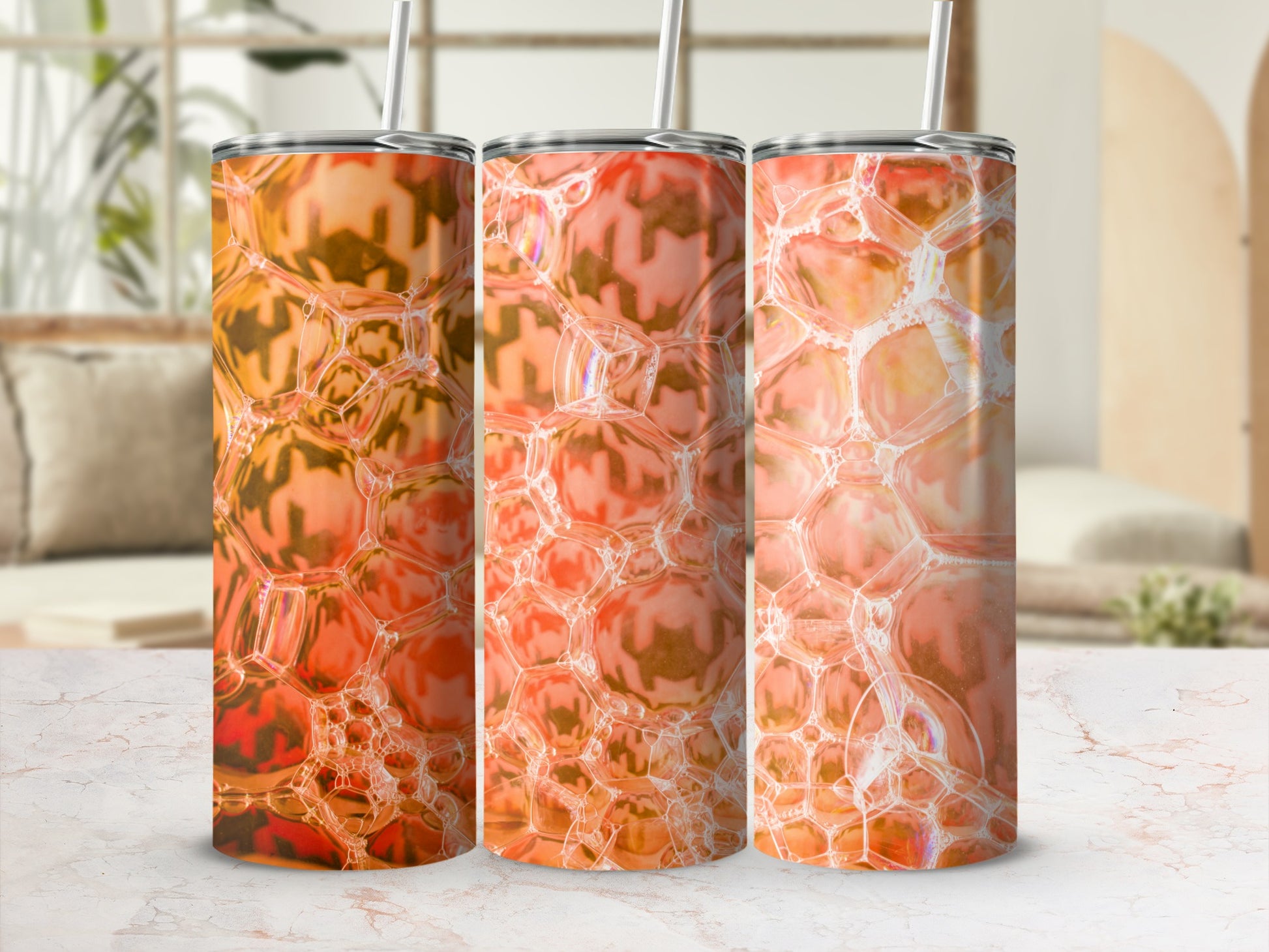 Three orange bubble pattern tumblers with straws on a marble surface.
