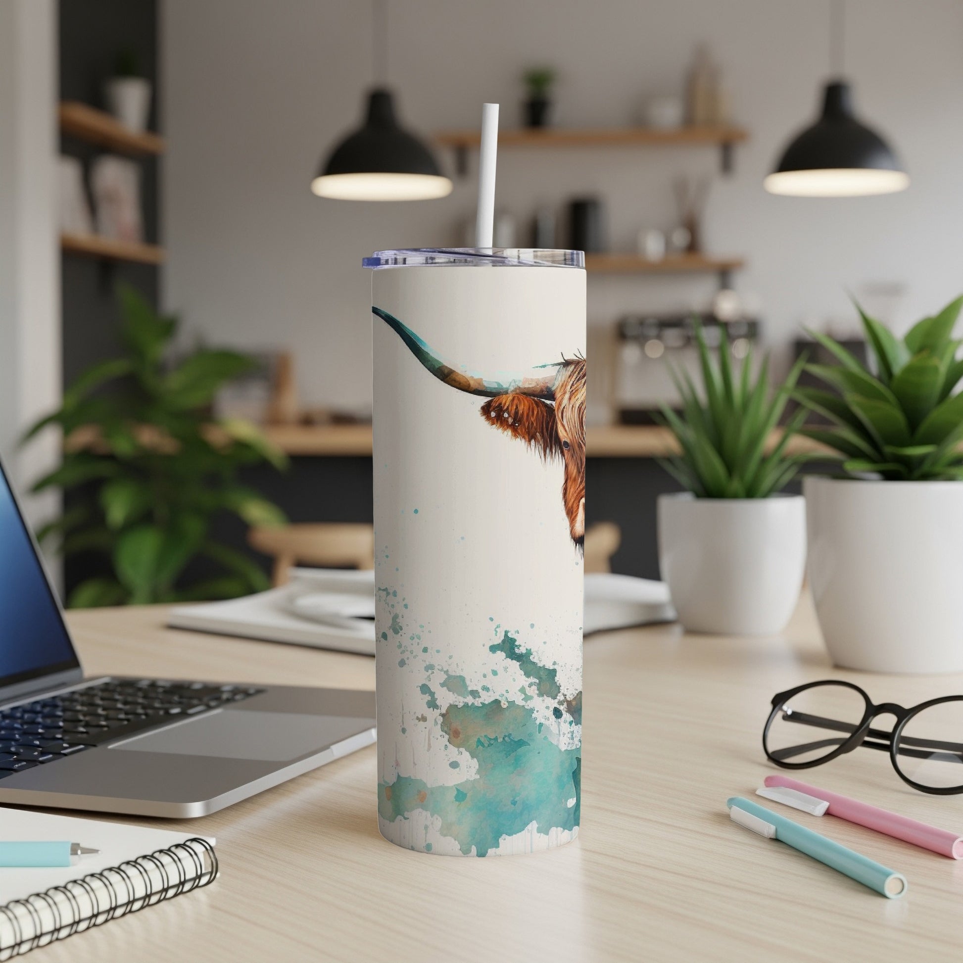 White tumbler with Highland cow watercolor design and straw on a desk.