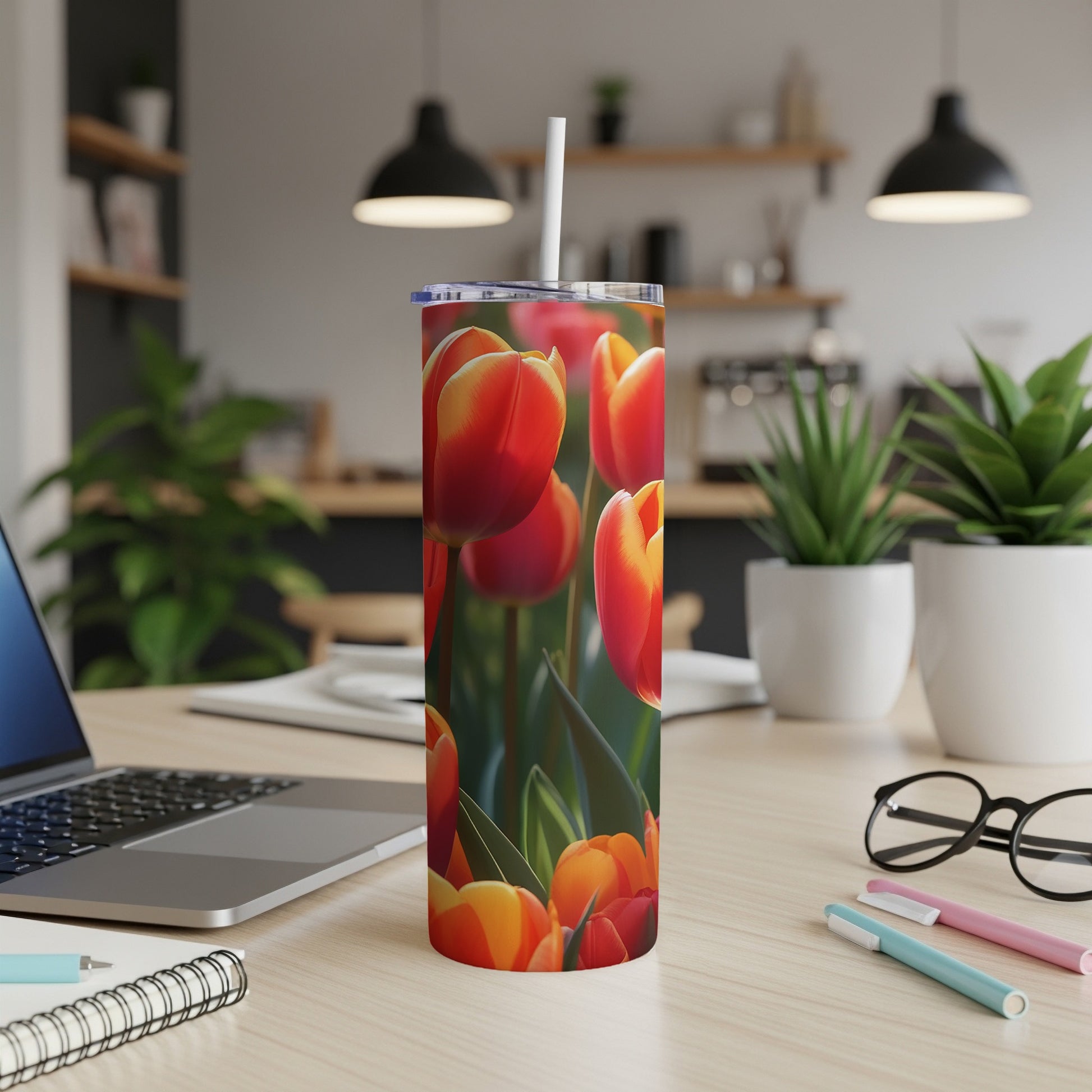 Tumbler with vibrant red and orange tulips, straw, laptop, and pens on desk.