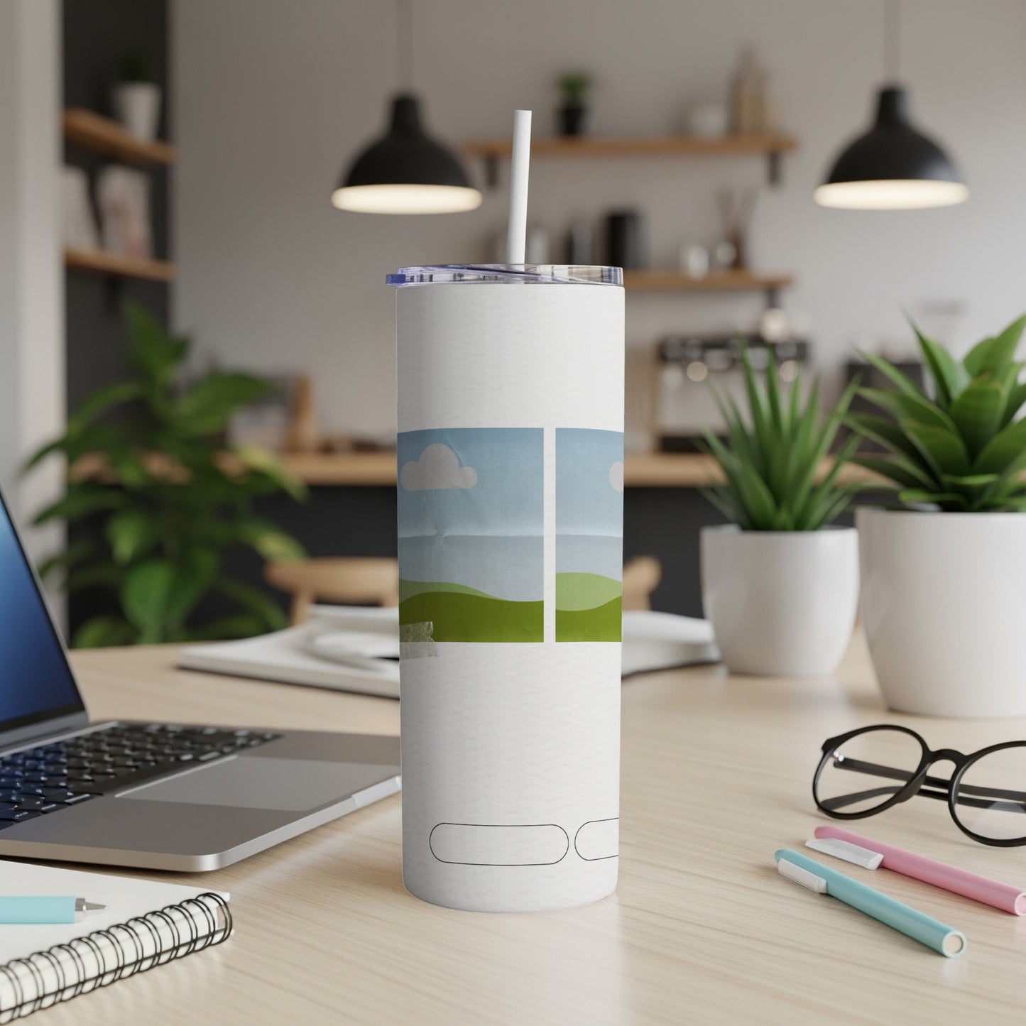 White tumbler with a landscape design and a straw on a desk.