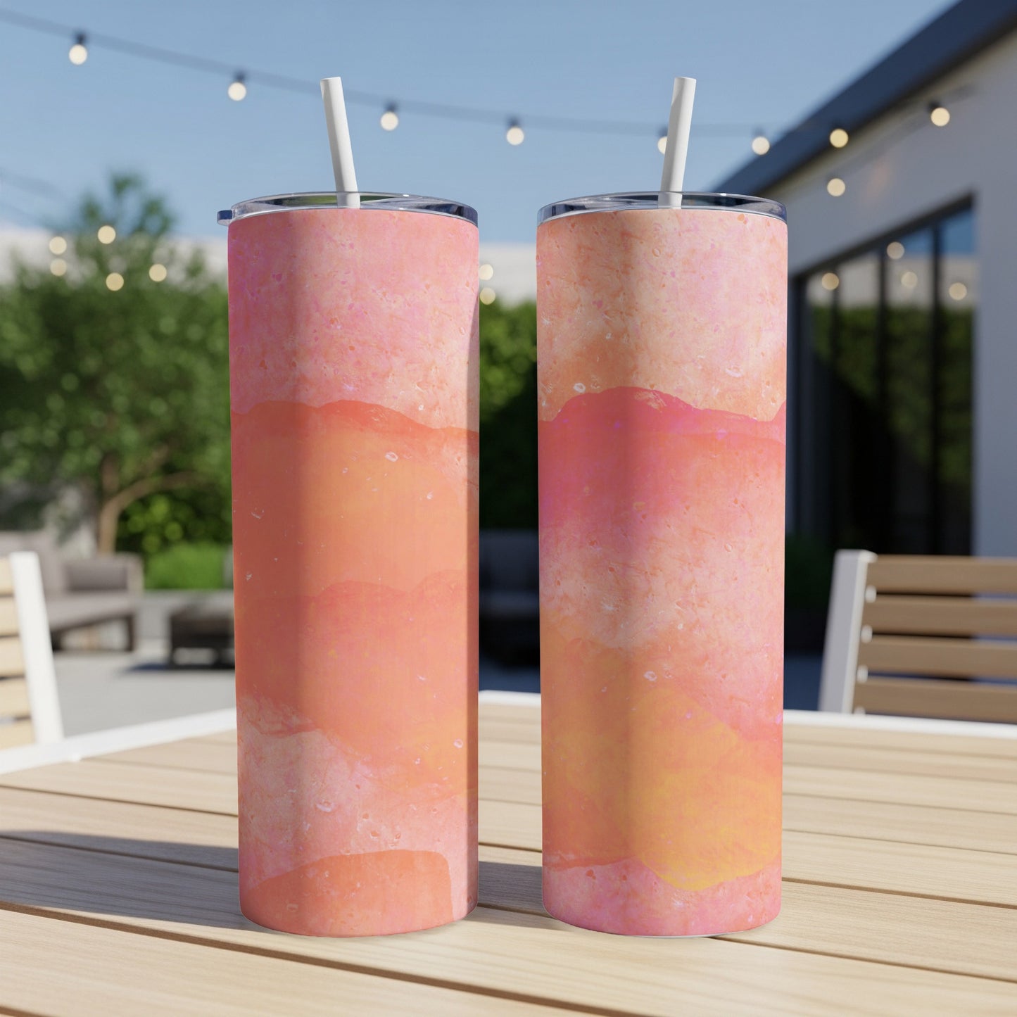 Two pink and orange textured tumblers with straws on a wooden table.
