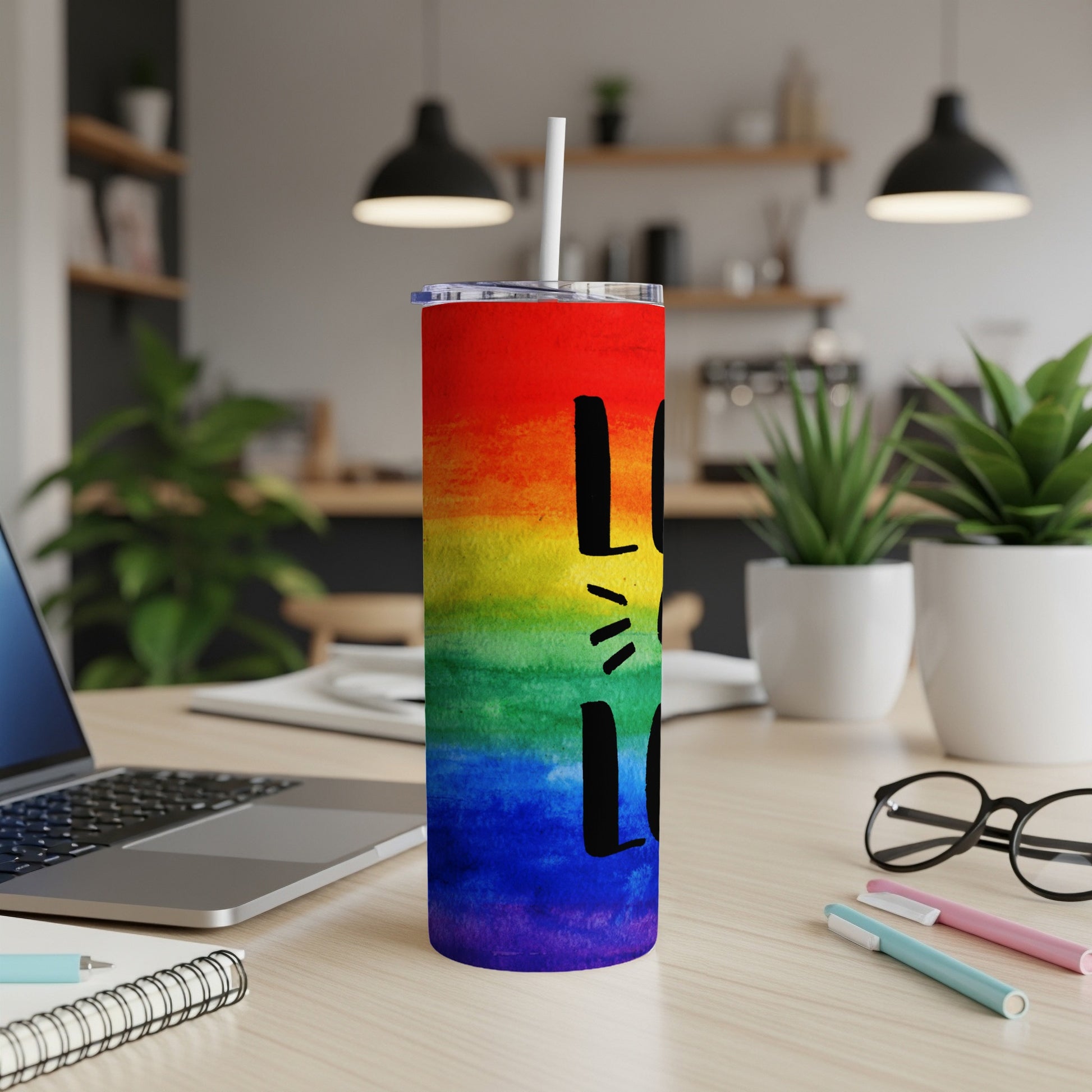 Rainbow tumbler with "love" text, on a desk with a laptop and plants.