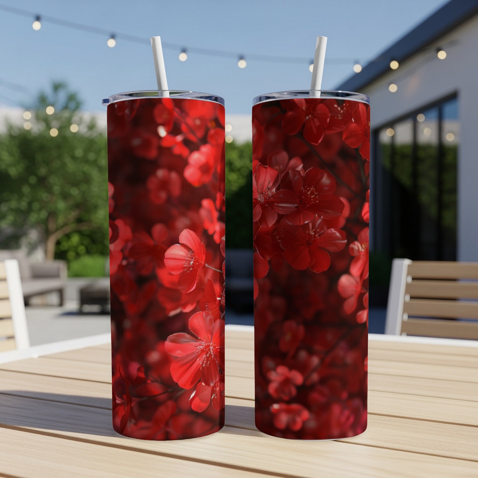 Two red floral print tumblers with straws on a wooden table outdoors.