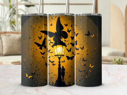 Three tumblers with a dark, glowing butterfly and silhouette design on a warm gradient background.