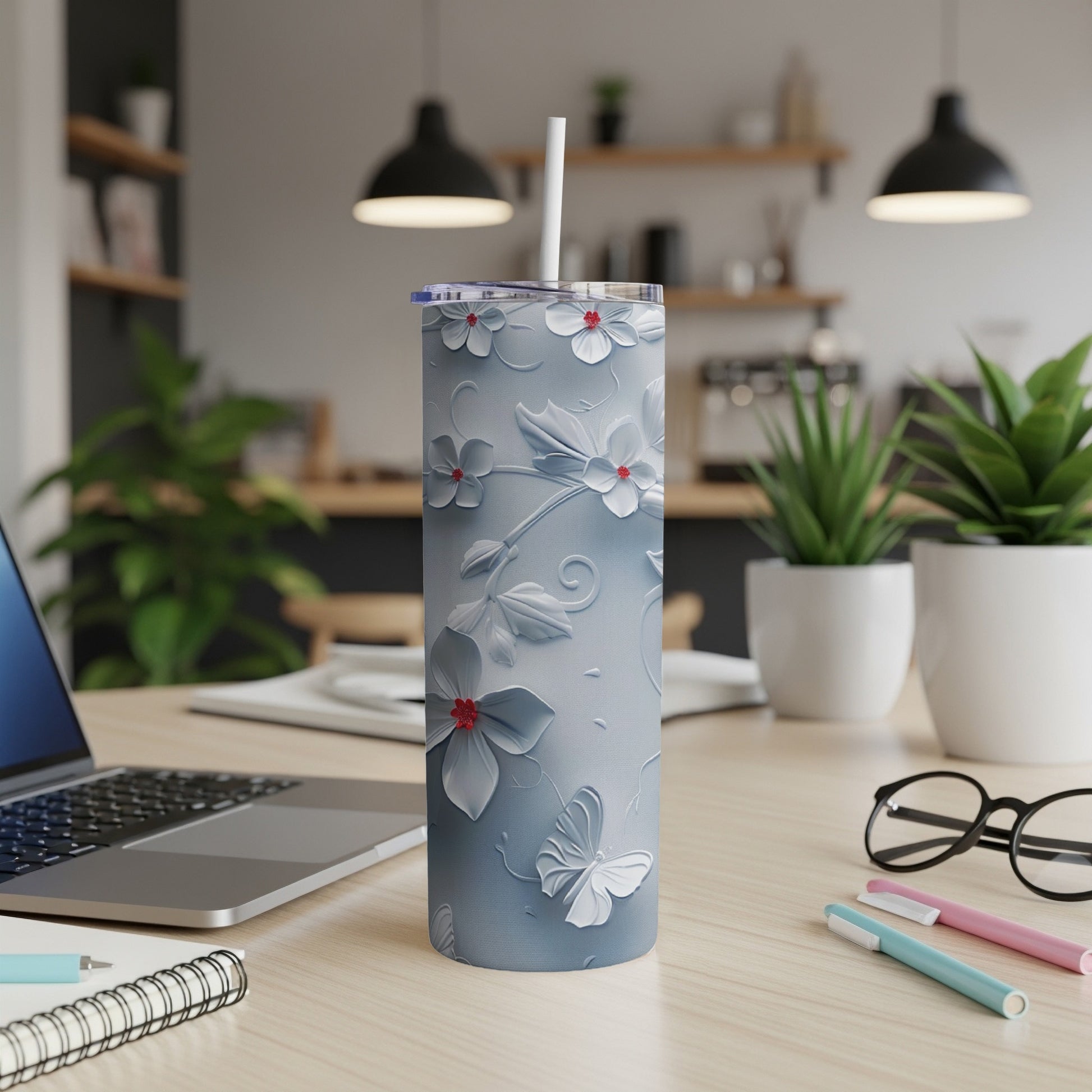 Light blue floral tumbler with straw on desk next to laptop and pens.