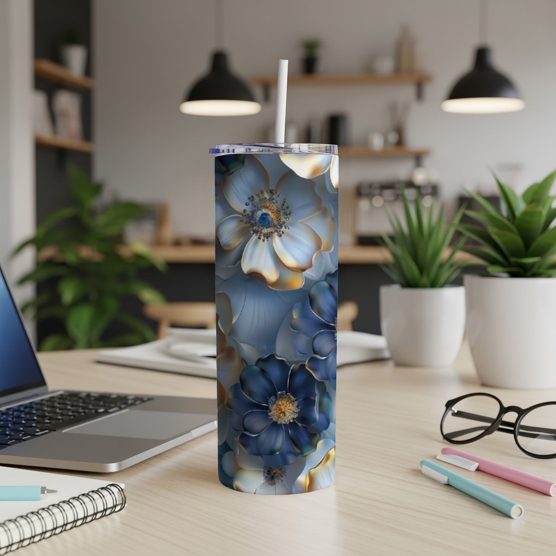 Blue floral pattern tumbler with straw on desk with laptop and pens.