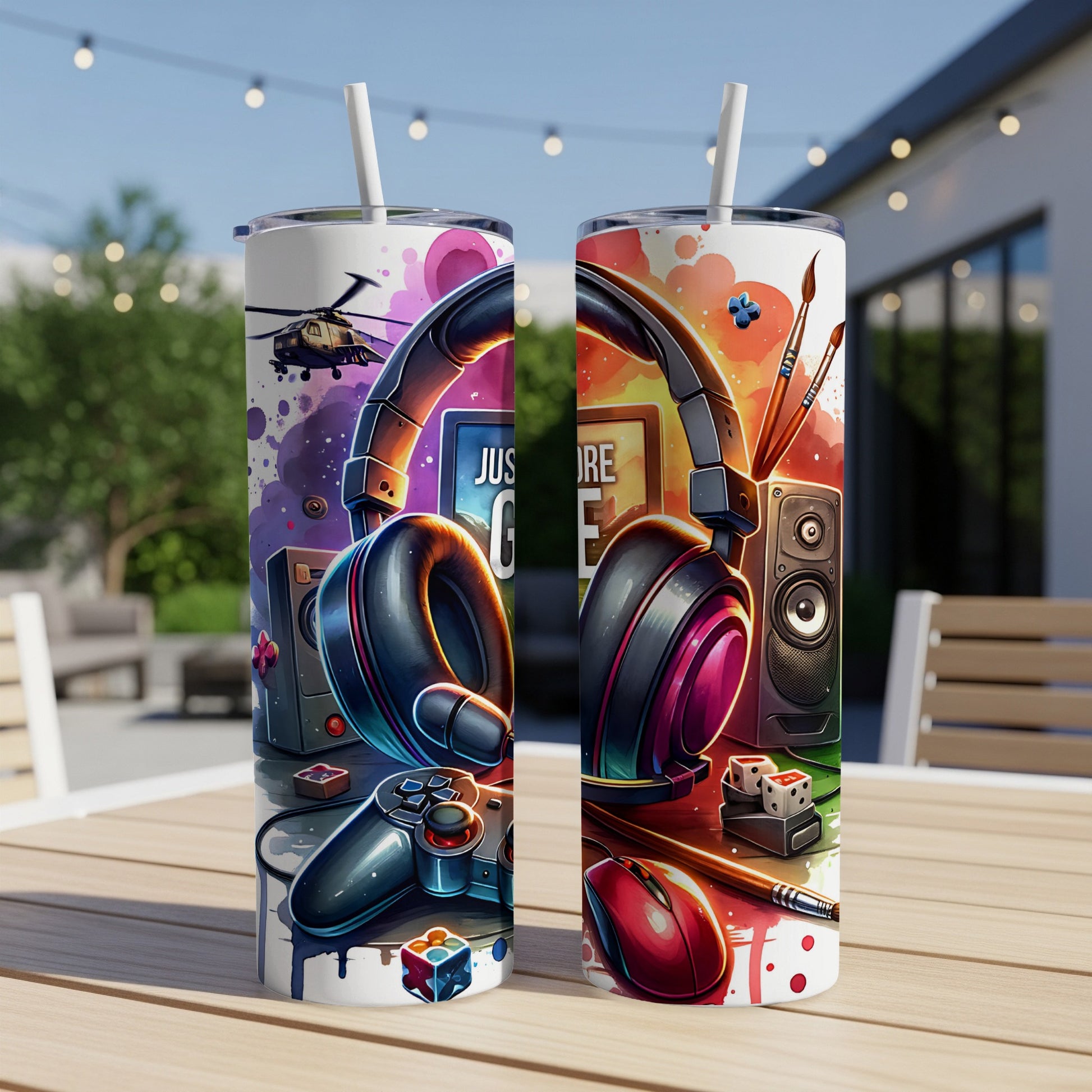 Two tumblers with gaming and art designs on a wooden table outdoors.