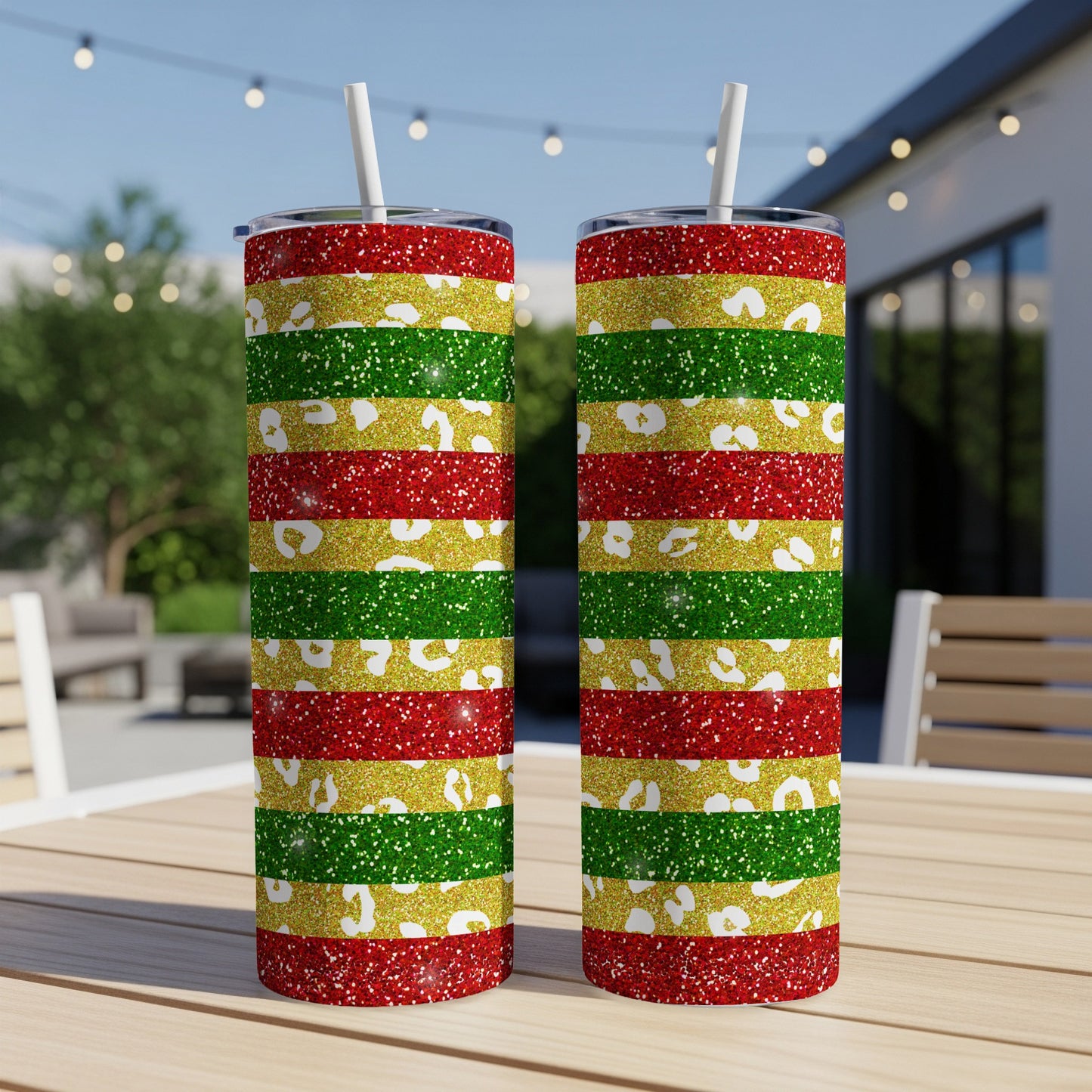 Two tumblers with red, green, and glitter stripes sit on a table outdoors.