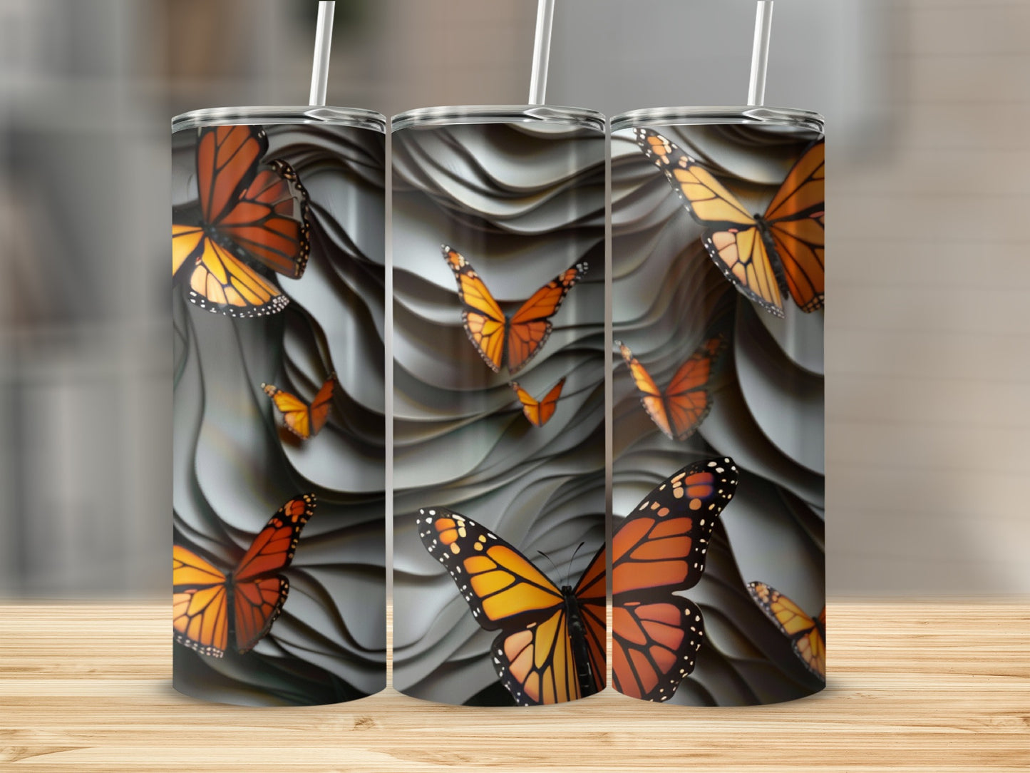 Three tumblers with orange monarch butterflies on a wavy gray background.