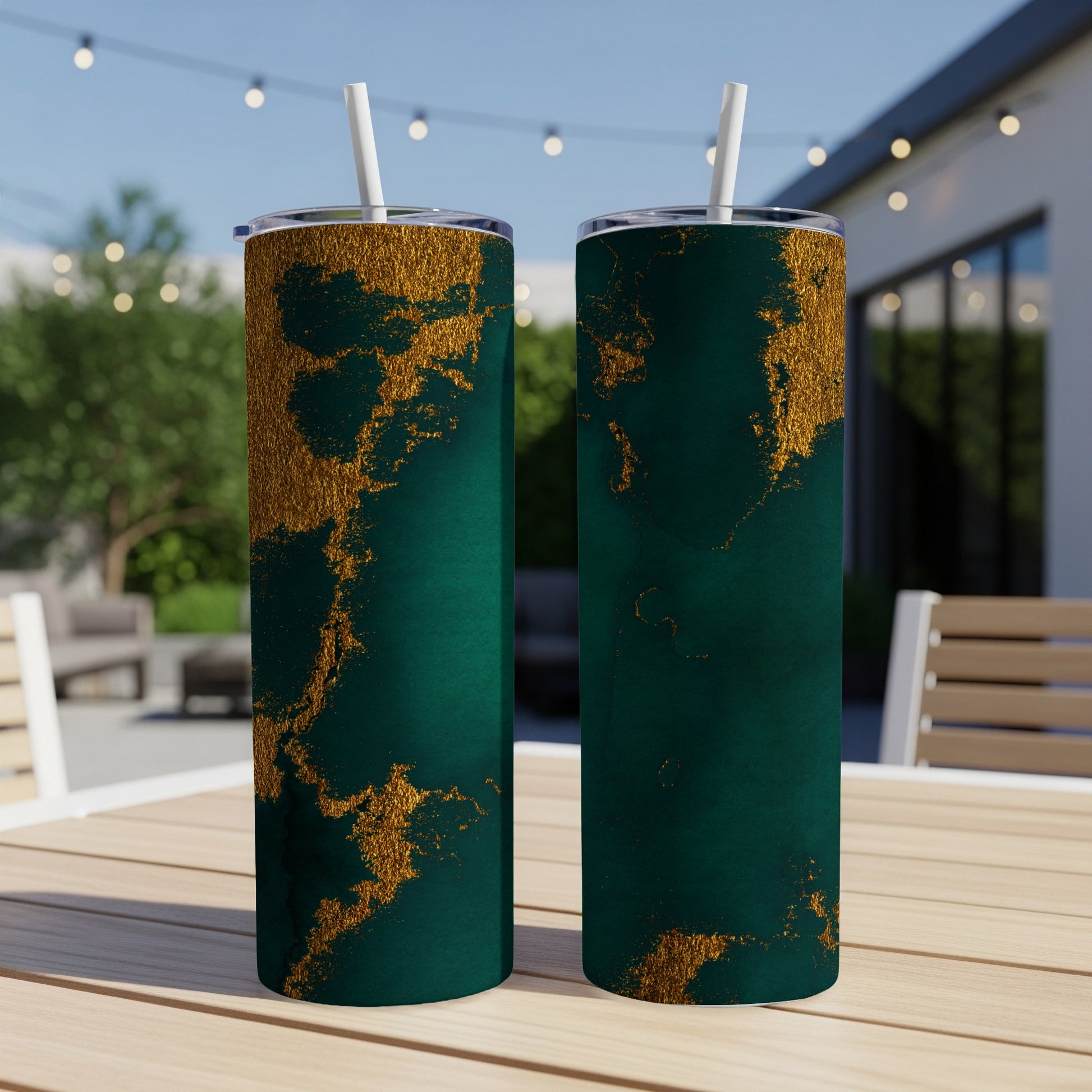 Two dark teal tumblers with gold marbling patterns and straws sit on a table.
