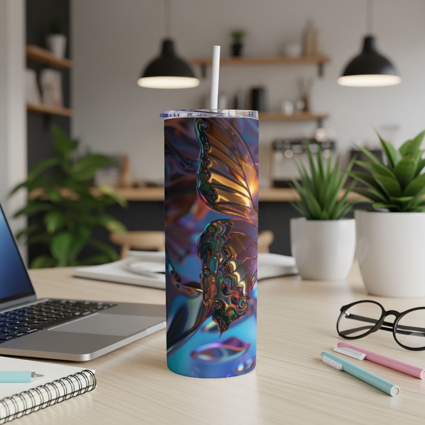 Tall tumbler with a metallic butterfly design rests on a desk with a laptop and pens.
