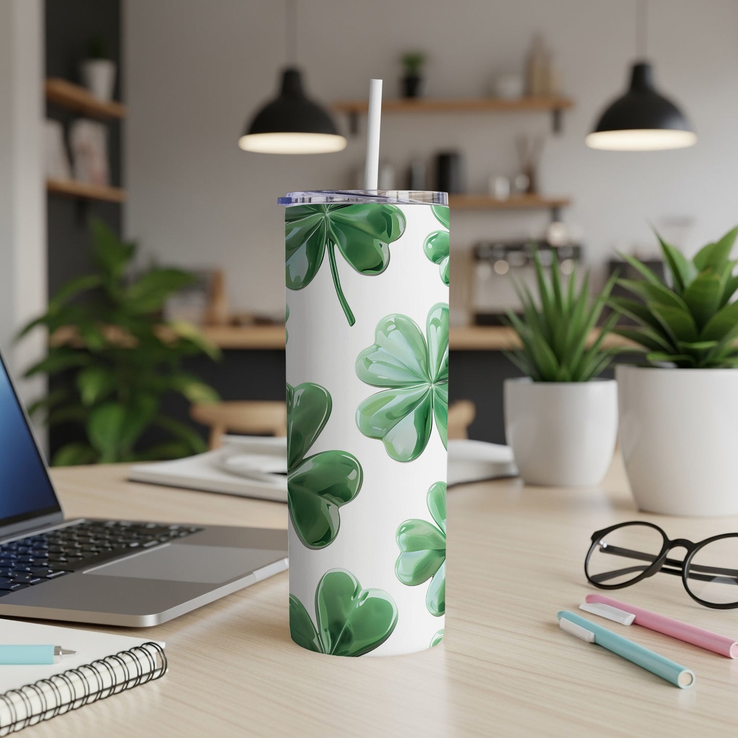 White tumbler with green shamrock pattern and straw on a desk.
