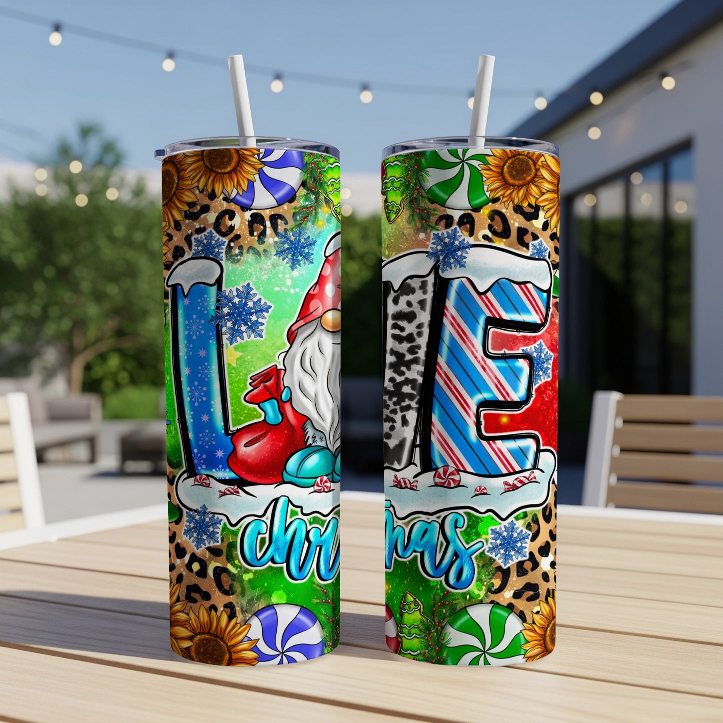 Two tumblers with a gnome and "LOVE Christmas" design on a wooden table outdoors.
