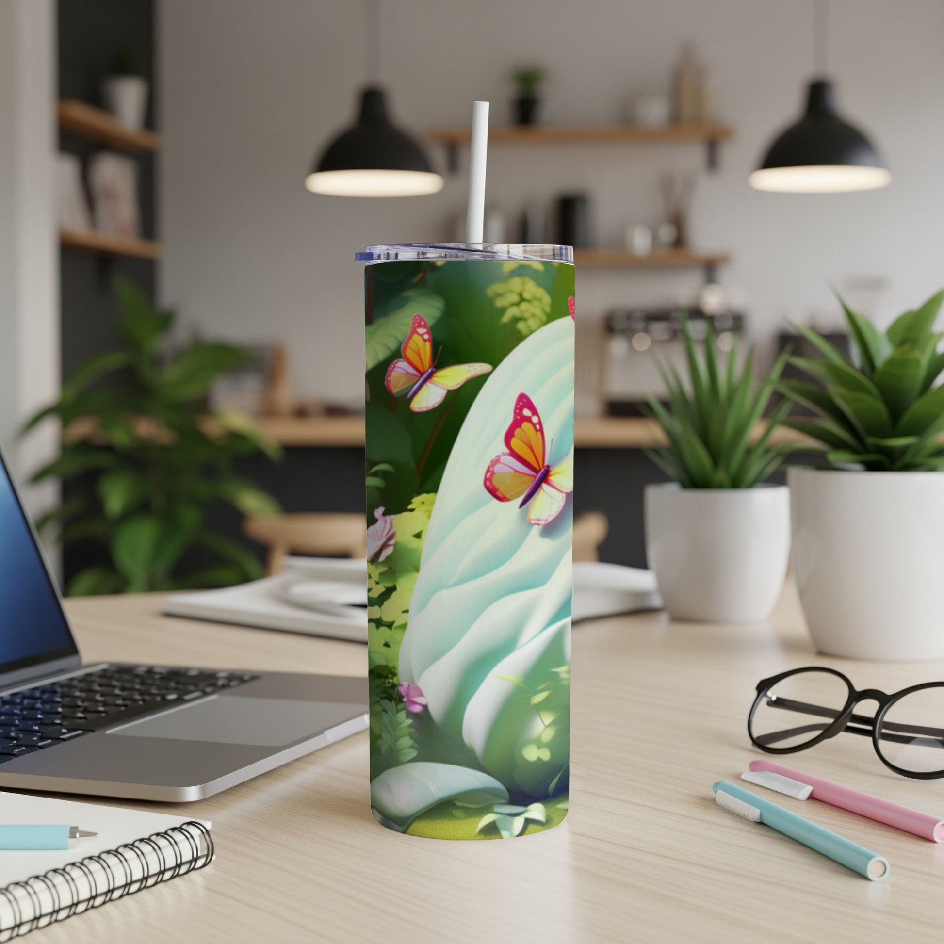 Floral tumbler with butterflies on a desk with a laptop and pens.
