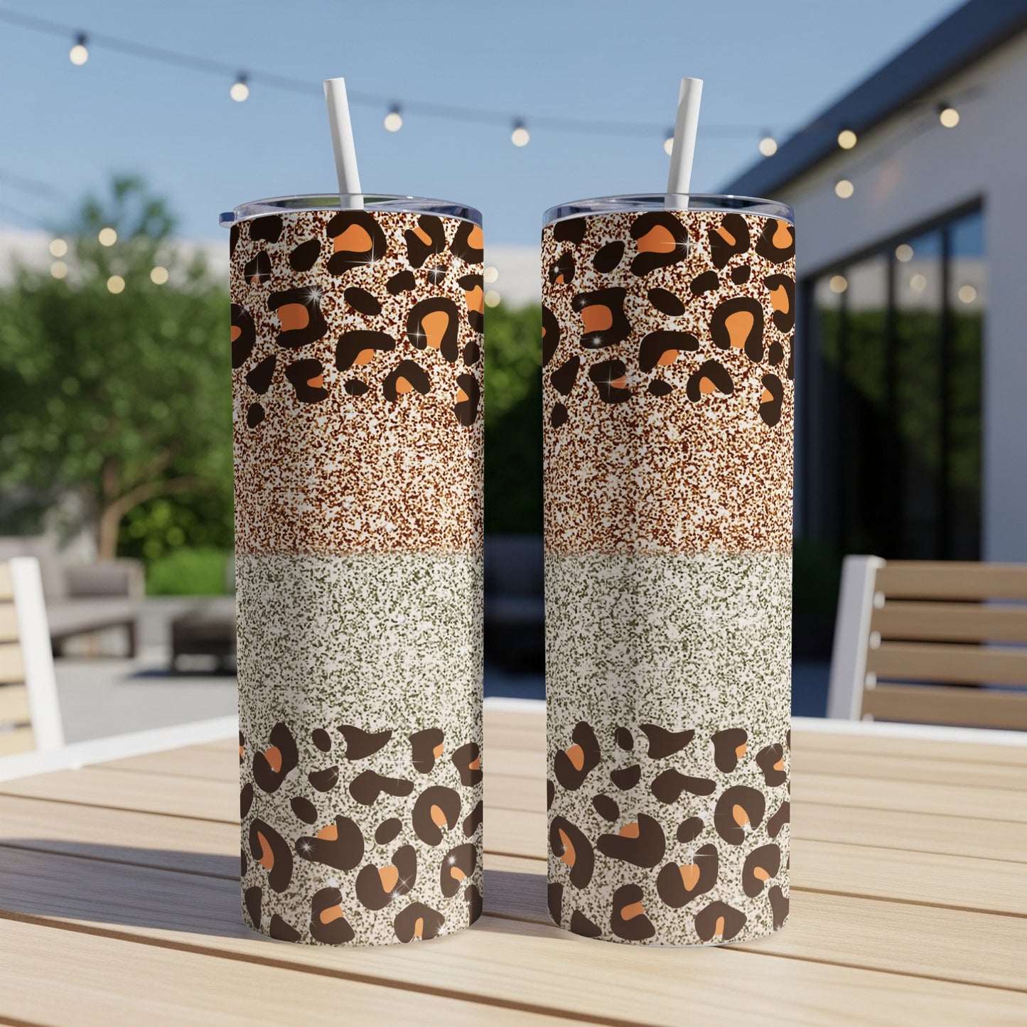 Two leopard print and glitter tumblers with straws on a table.