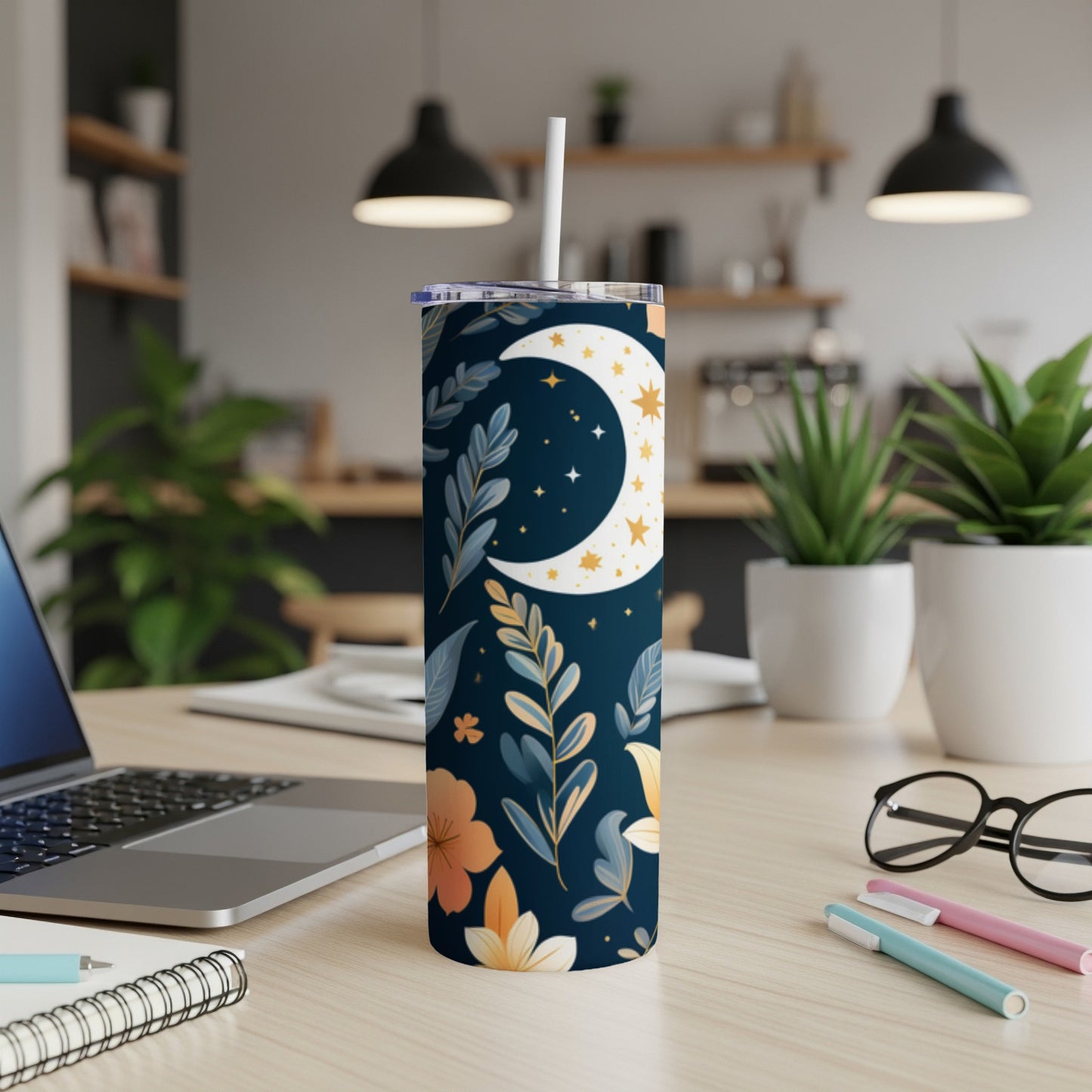 Dark blue tumbler with celestial moon and floral pattern, on a desk.