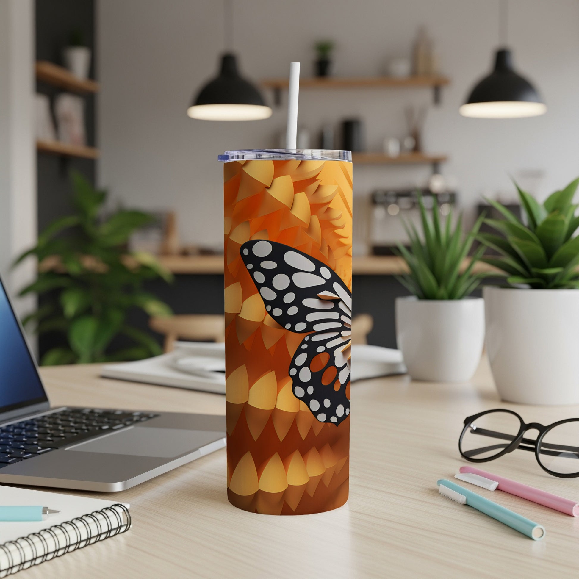 Tall tumbler with a butterfly design and straw on a desk.
