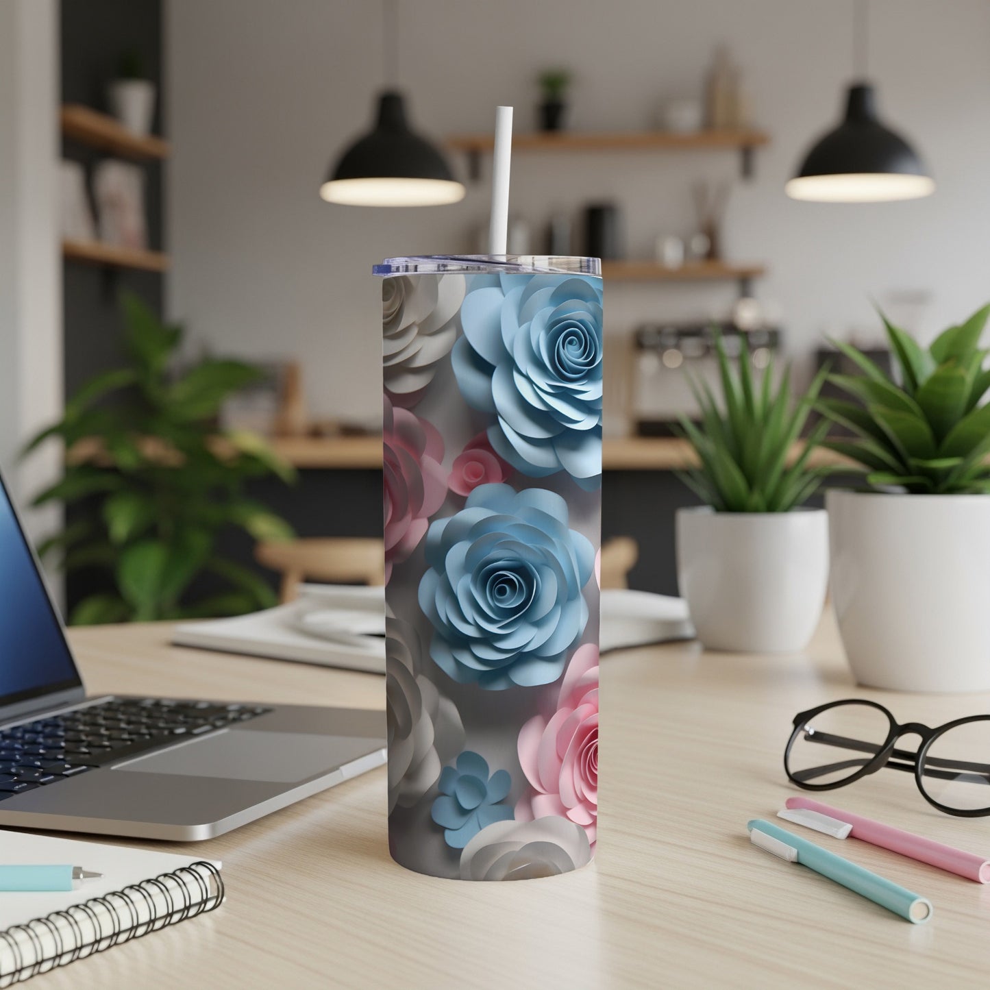 Floral patterned tumbler with straw on desk, laptop, and pens.