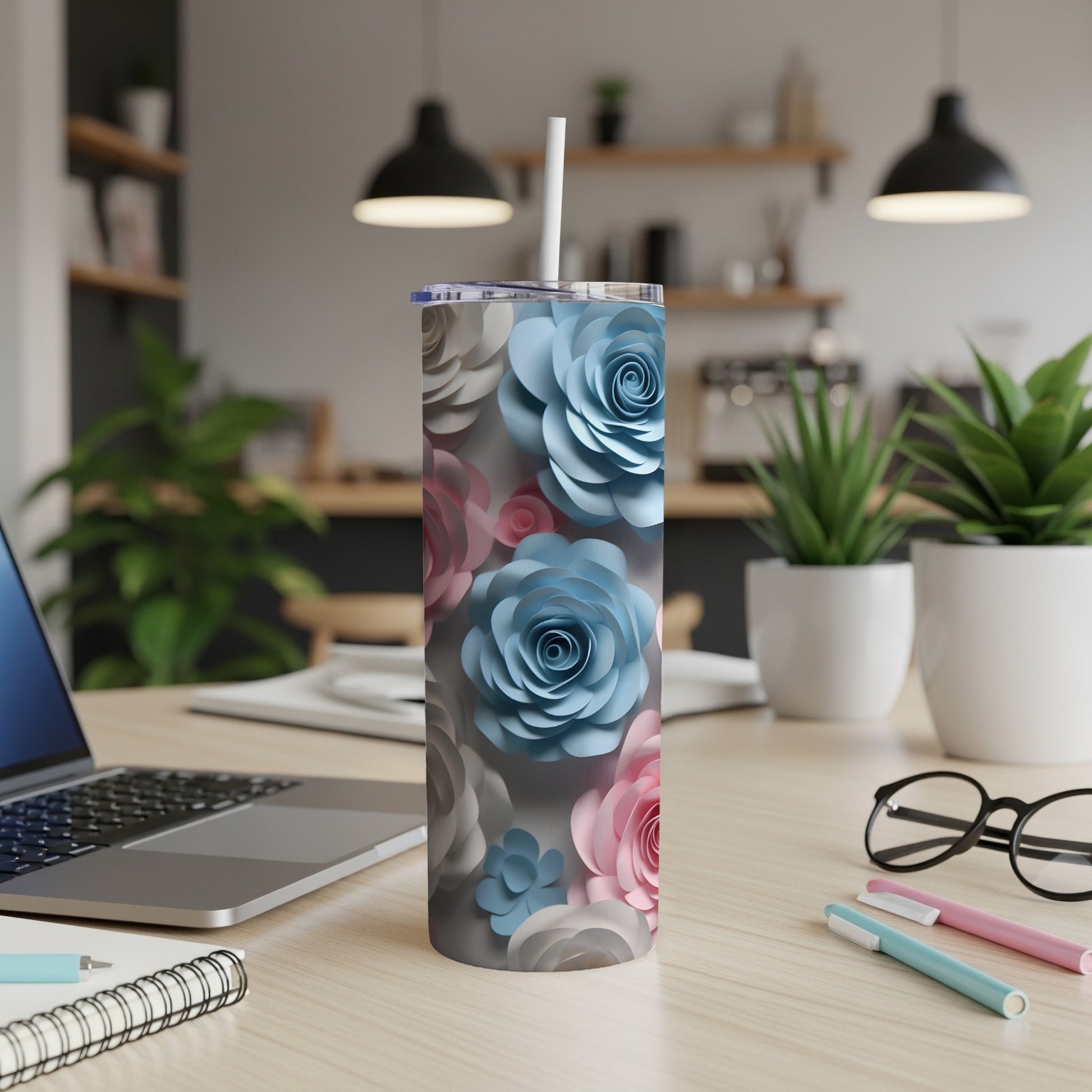 Floral patterned tumbler with straw on desk, laptop, and pens.