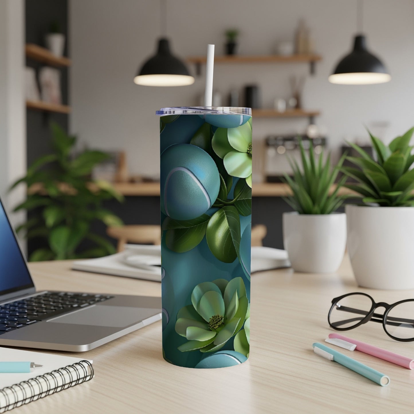 Teal tumbler with tennis balls and leaves design on a desk.