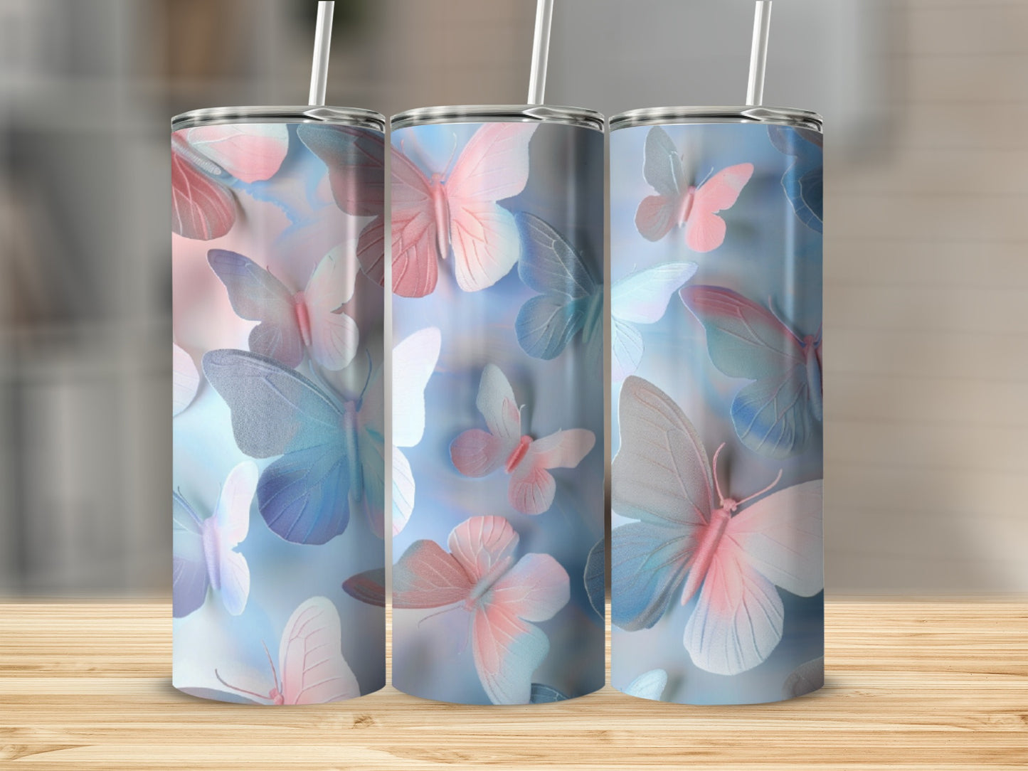 Three tumblers with pastel butterfly designs and straws on a wooden surface.
