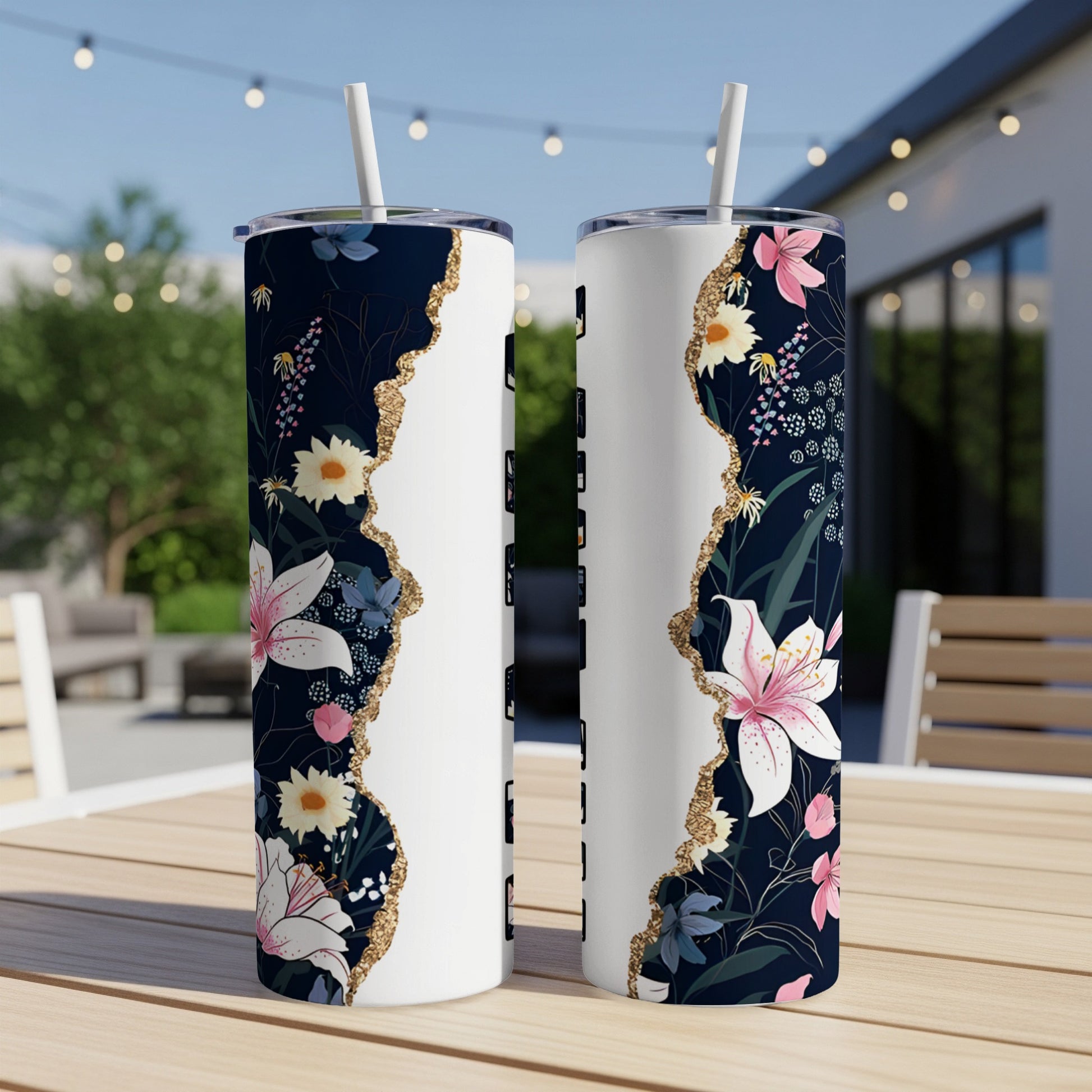 Two white tumblers with floral design and gold accents on outdoor table.