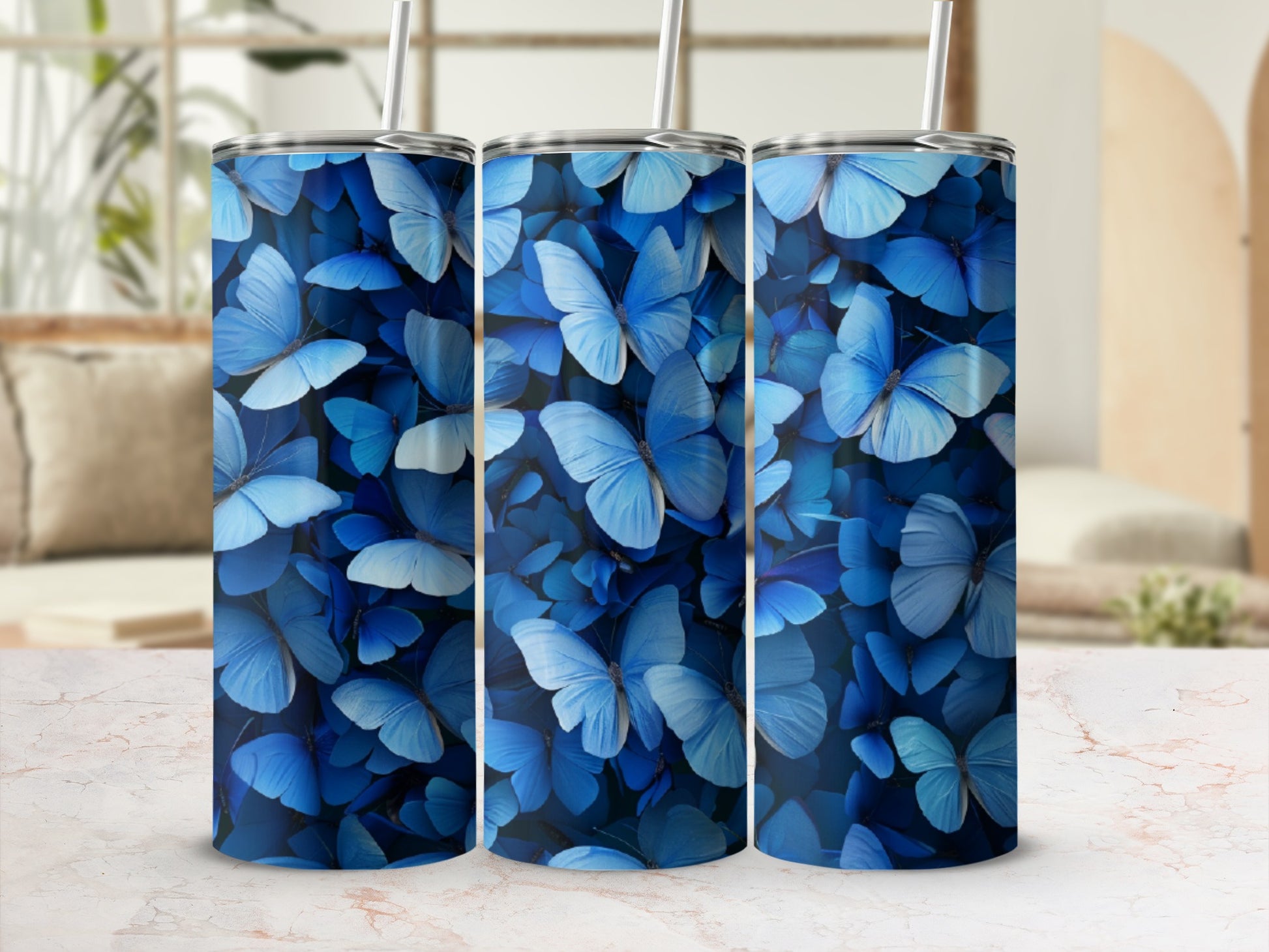 Three blue butterfly print tumblers on a marble surface with blurred background.