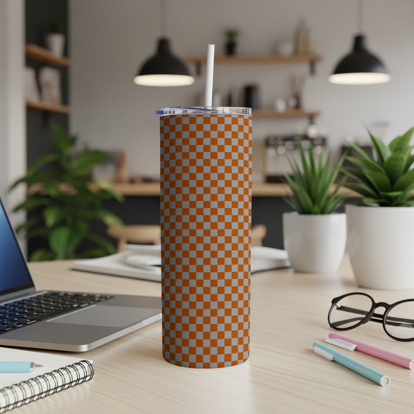 Orange and gray checkered tumbler with a white straw on a desk.