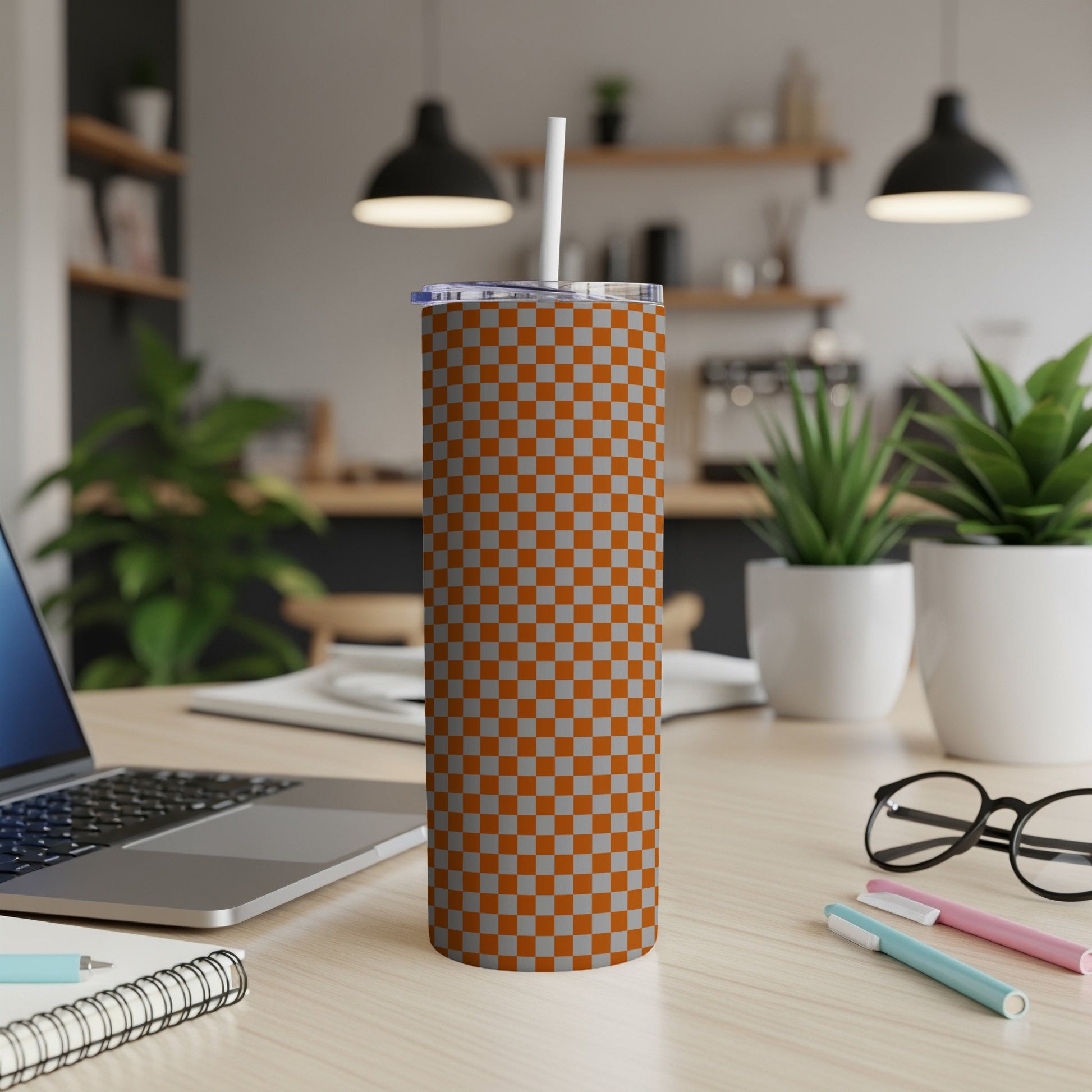 Orange and gray checkered tumbler with a white straw on a desk.