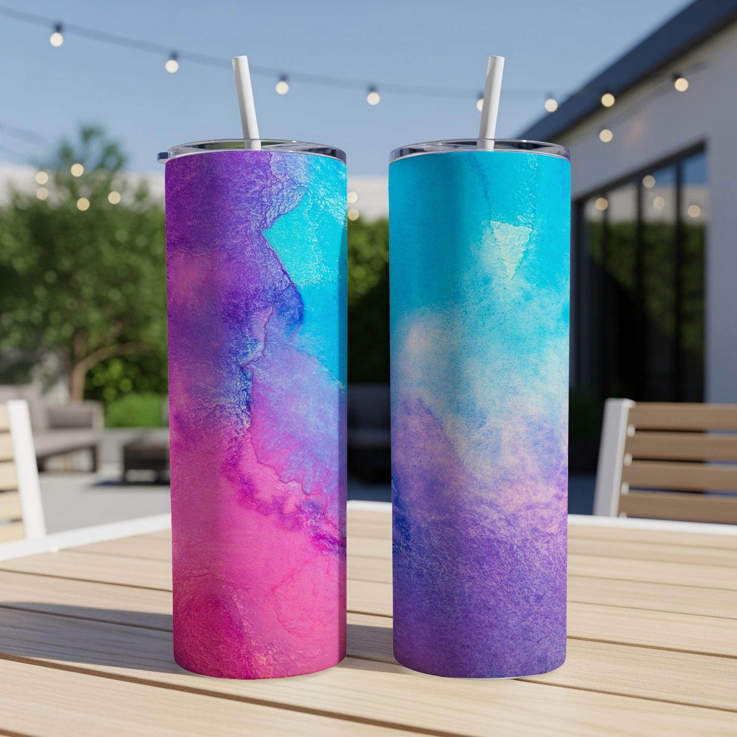 Two tumblers with pink, purple, and blue watercolor designs on a table.
