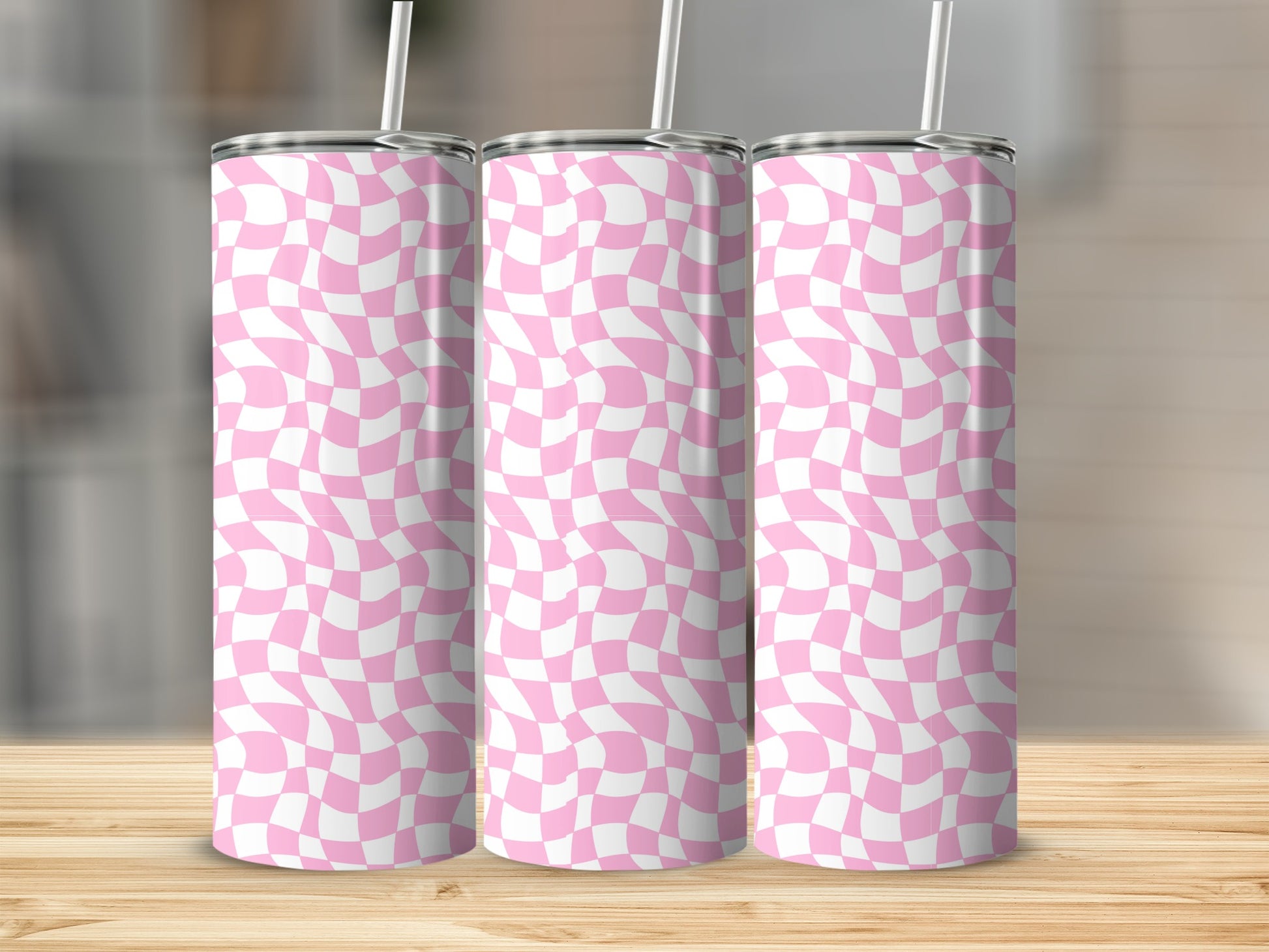 Three pink and white checkered tumblers with straws on a wooden surface.