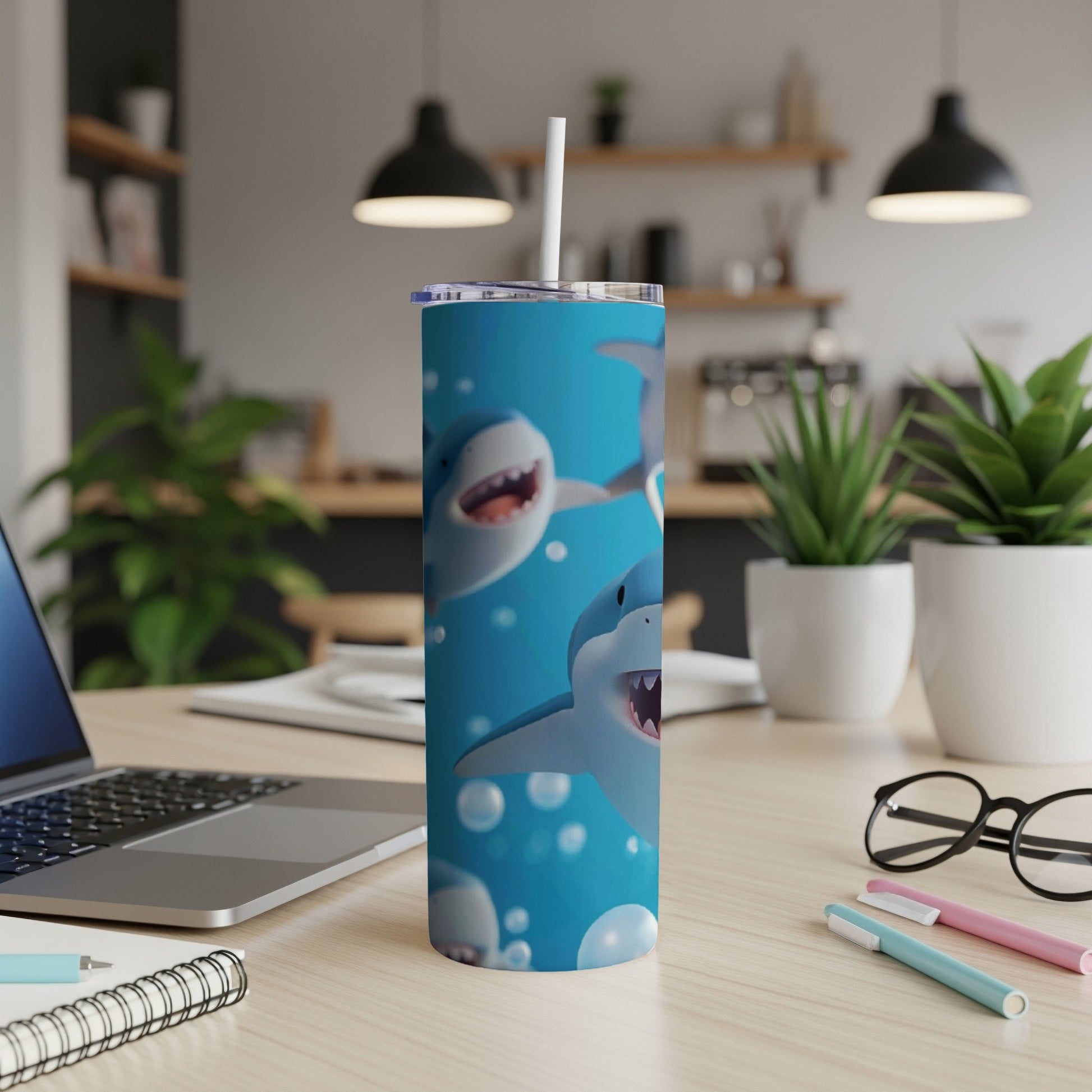 Blue tumbler with cartoon sharks and bubbles, on a desk with a laptop.