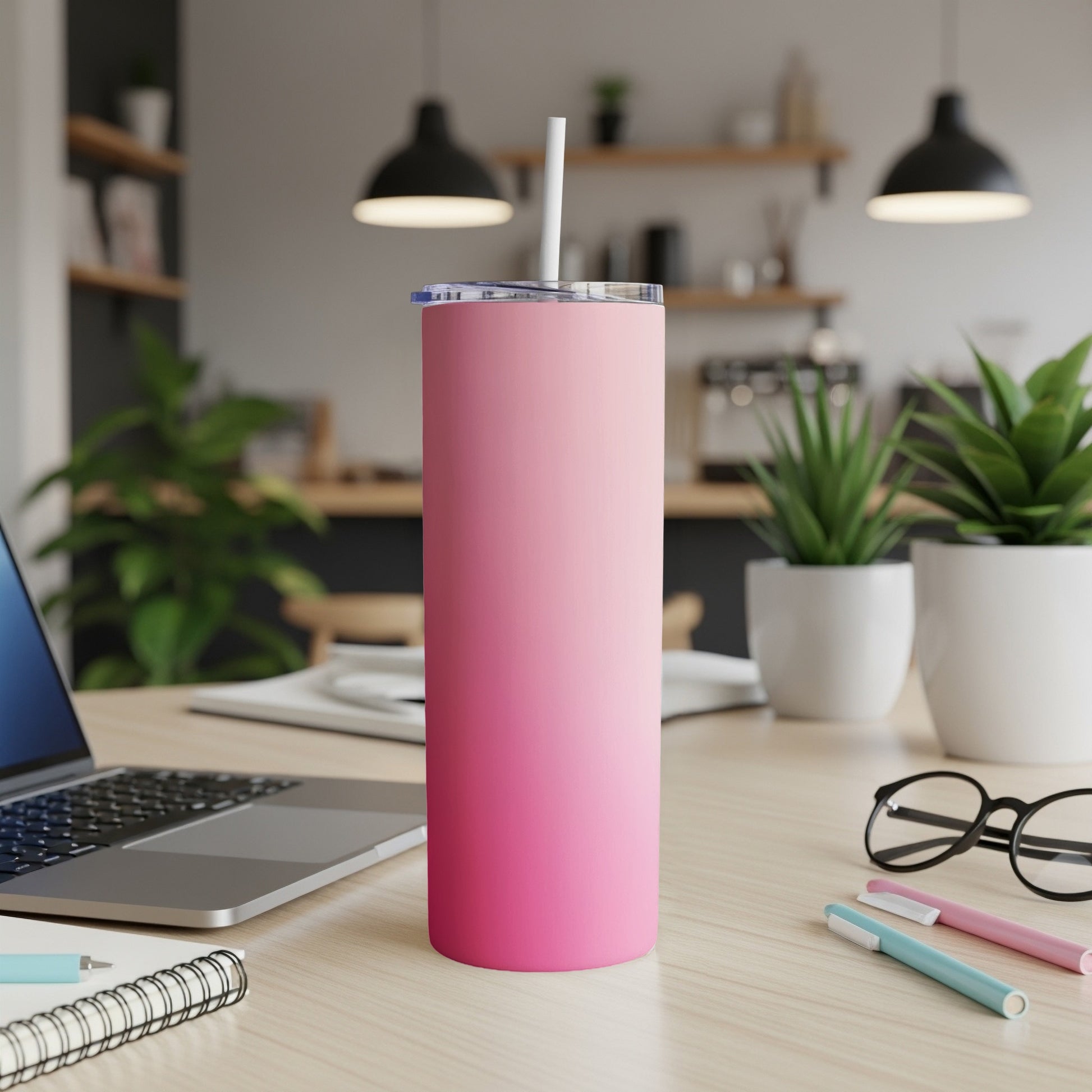Pink gradient tumbler with straw on a desk next to a laptop.