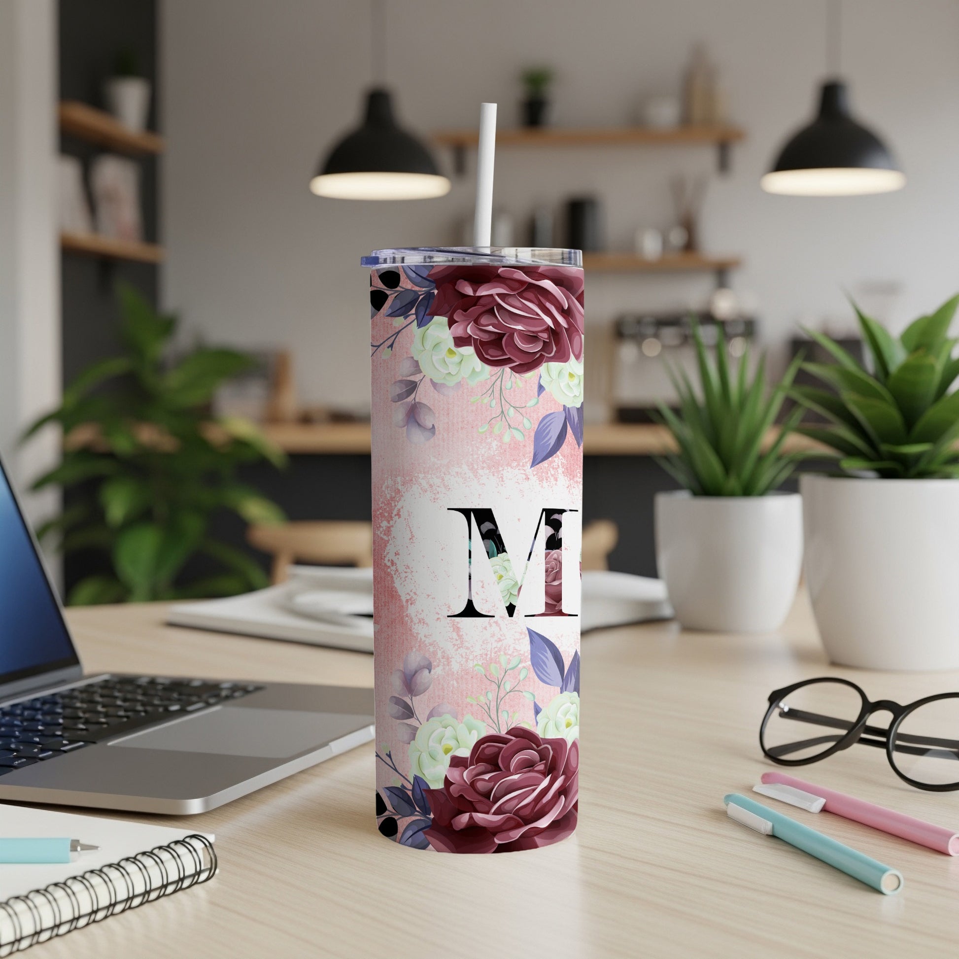 Pink floral tumbler with a large initial "M" on a desk.