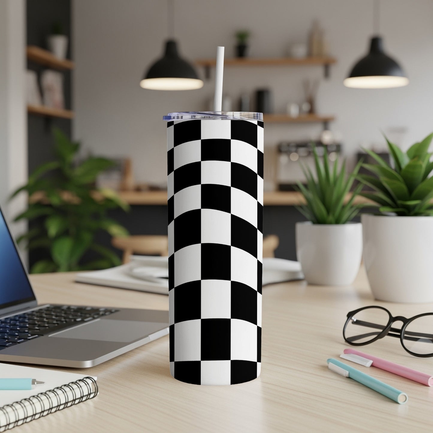 Black and white checkered tumbler on a desk with a laptop and pens.
