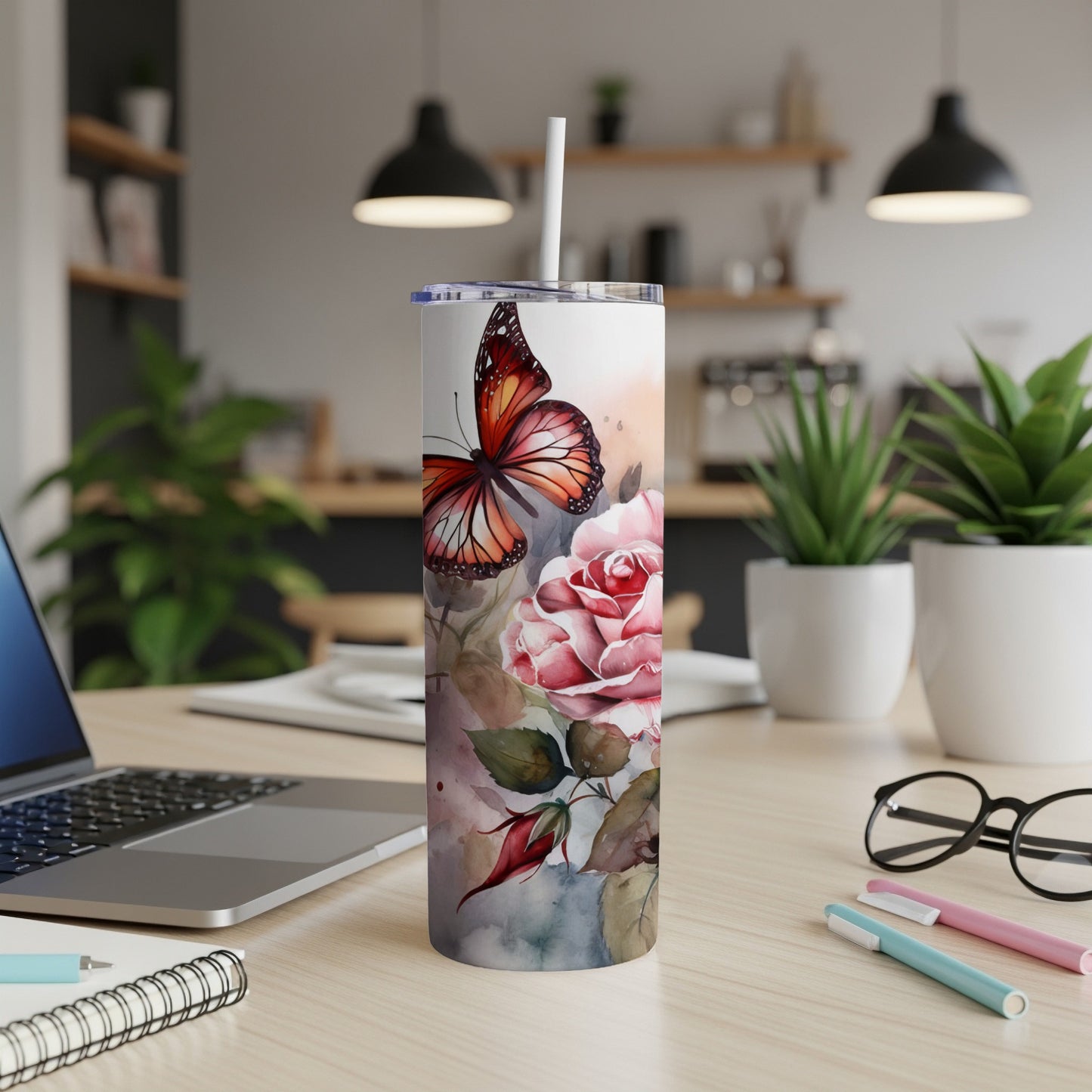 Tumbler with butterfly and roses design, on a desk.