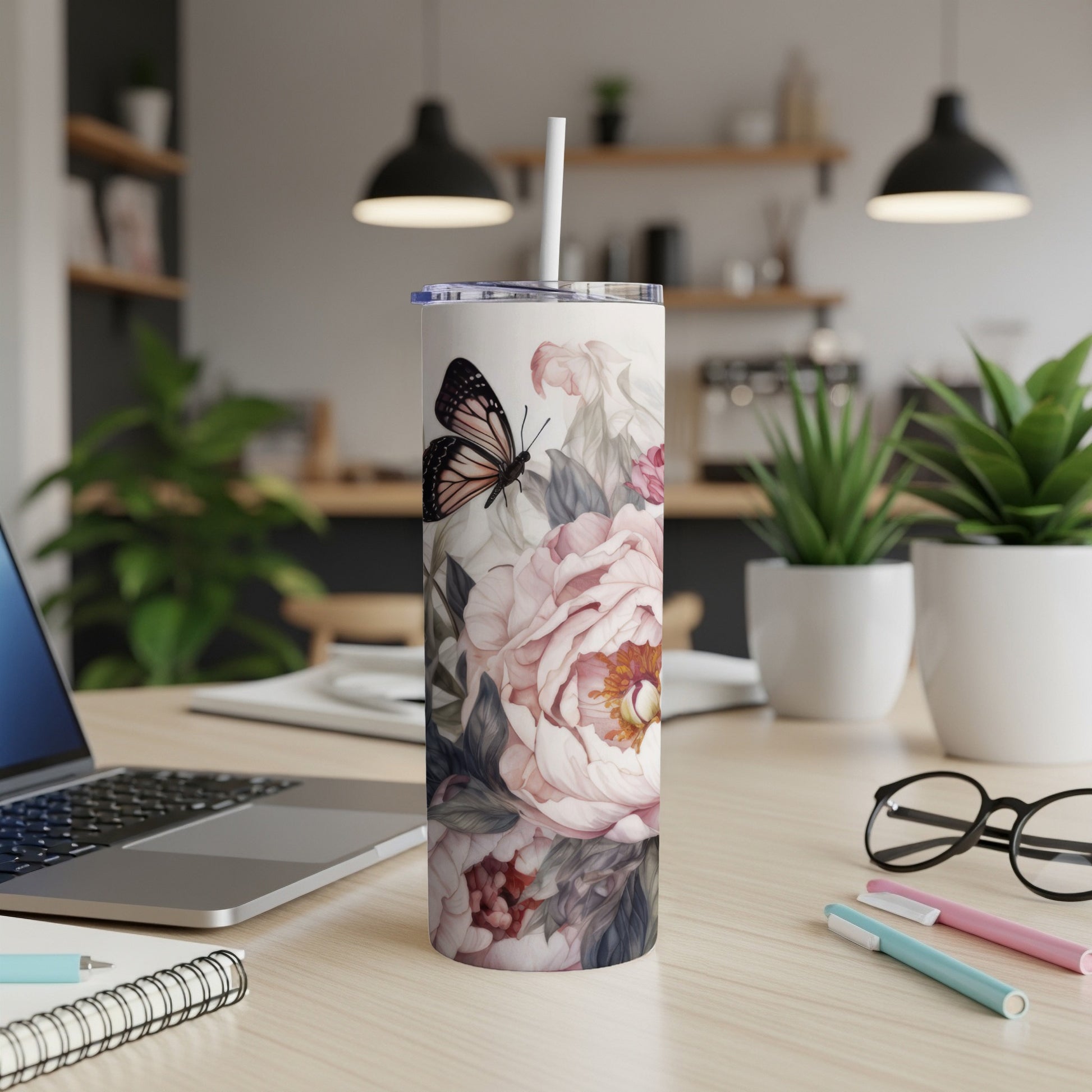 Floral tumbler with butterfly, white lid, and straw on a wooden desk.