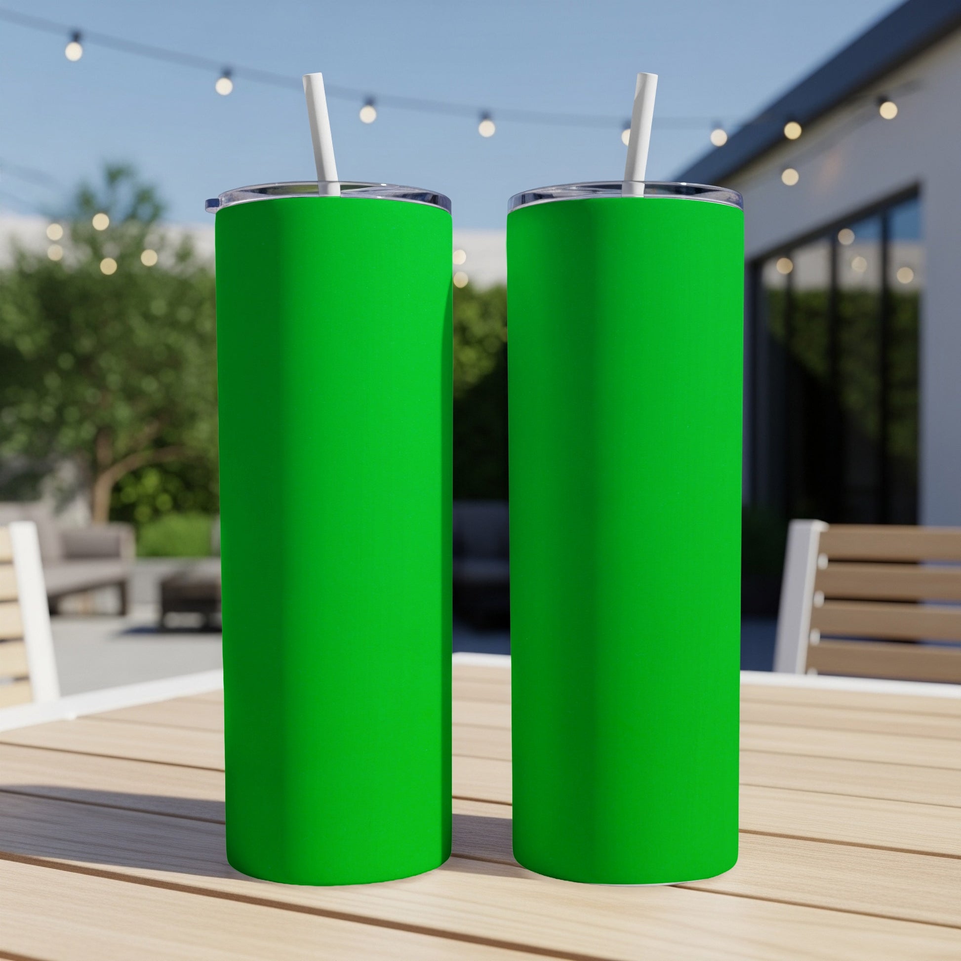 Two green tumblers with white straws on a wooden table outdoors.