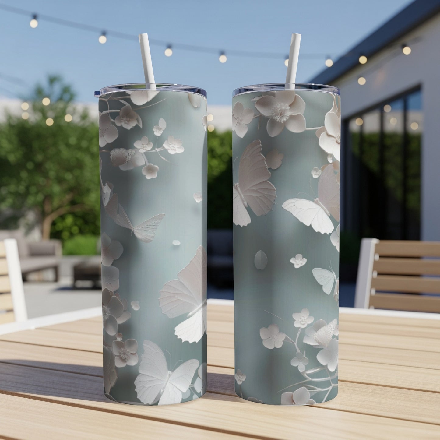 Two light blue tumblers with white butterflies and floral design on outdoor table.