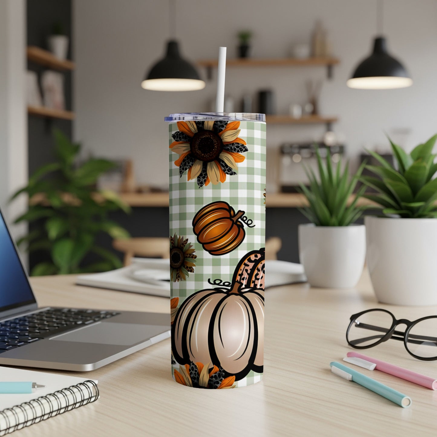 Gingham pumpkin and sunflower tumbler with straw on desk.