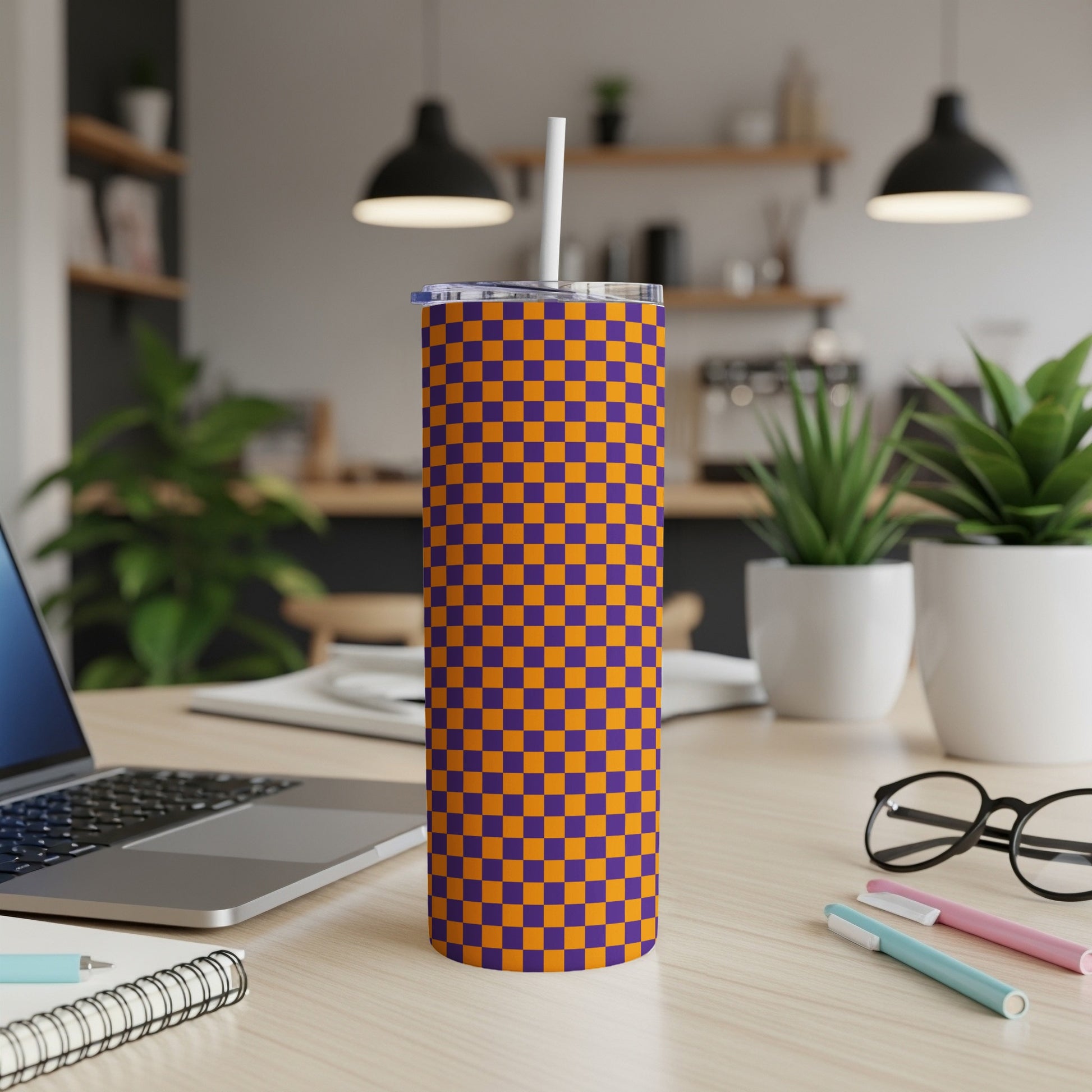 Orange and purple checkered tumbler with straw on a desk.