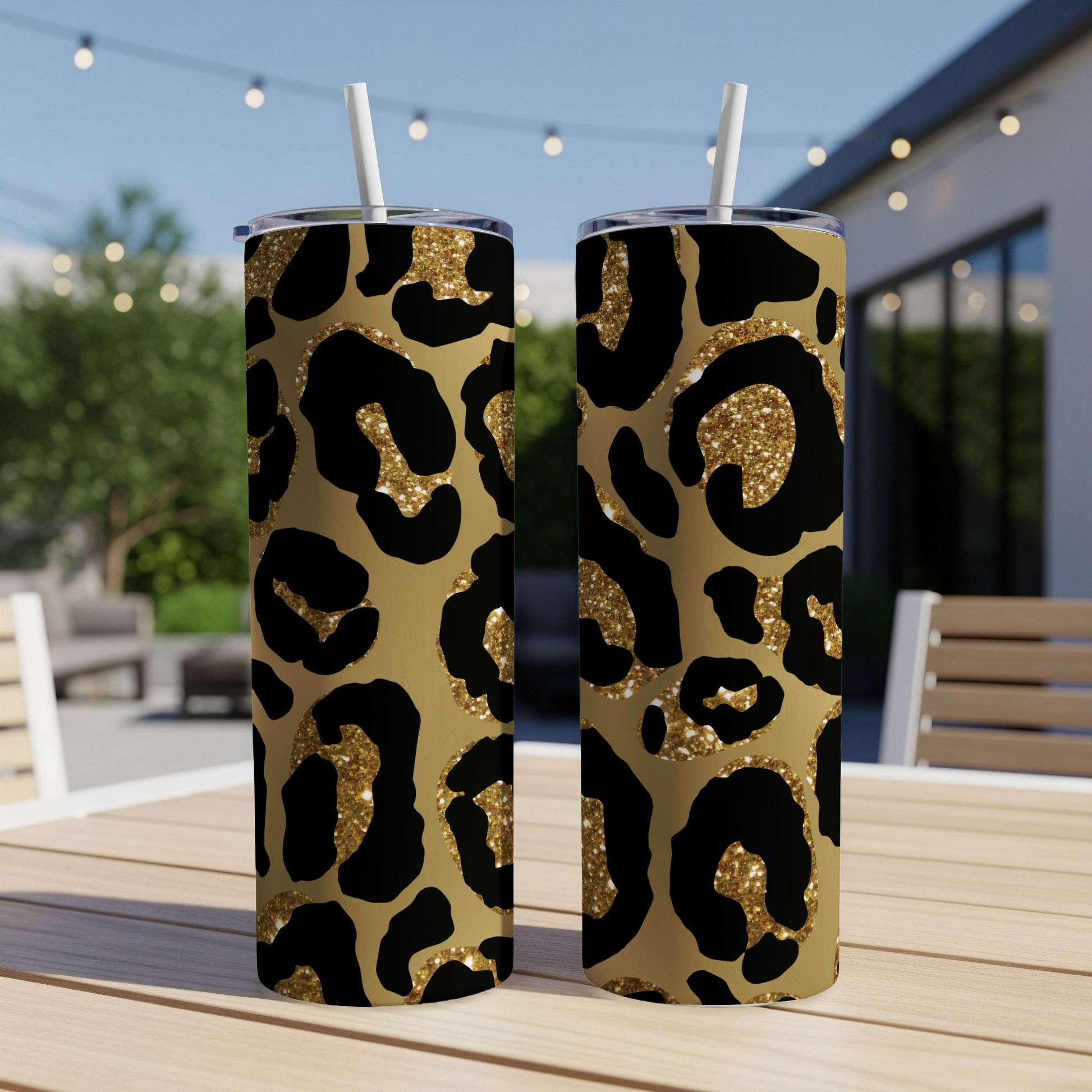 Two tall tumblers with gold leopard print and glitter accents sit on a wooden table.