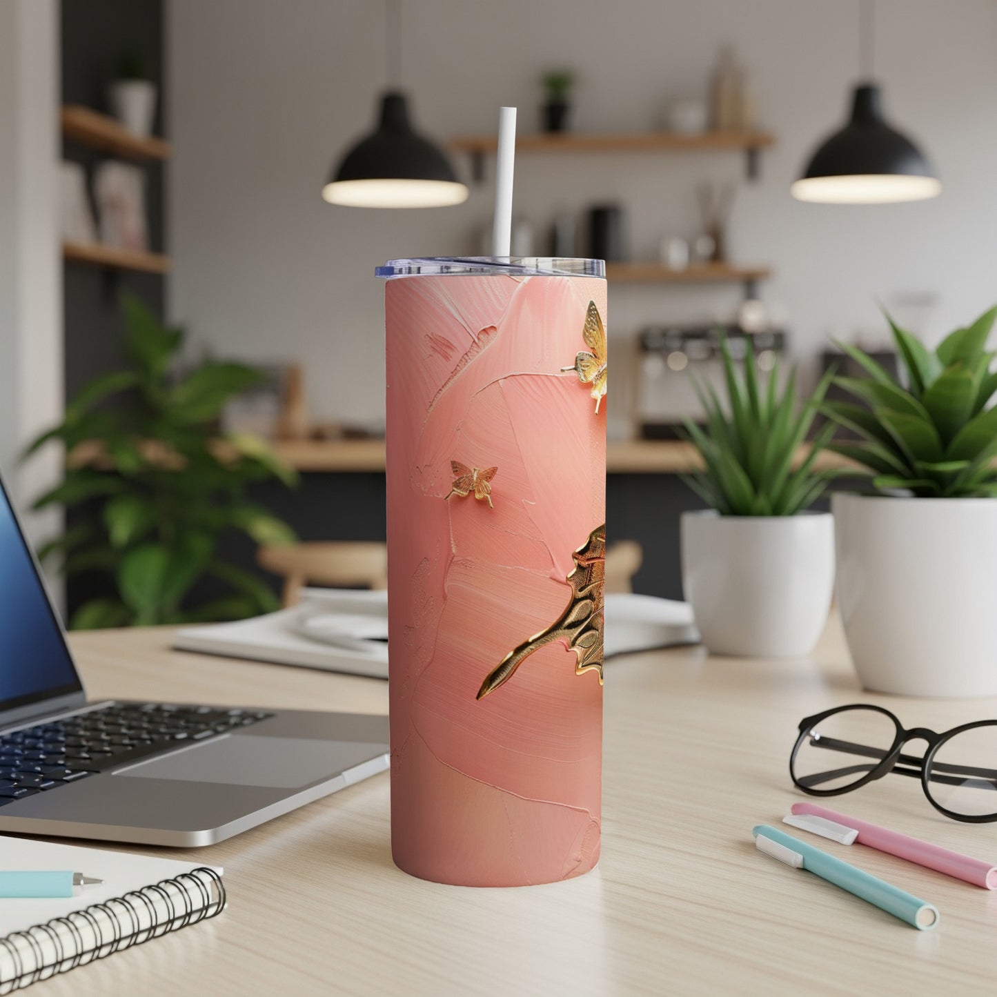 Pink textured tumbler with gold butterfly accents and a straw on a desk.