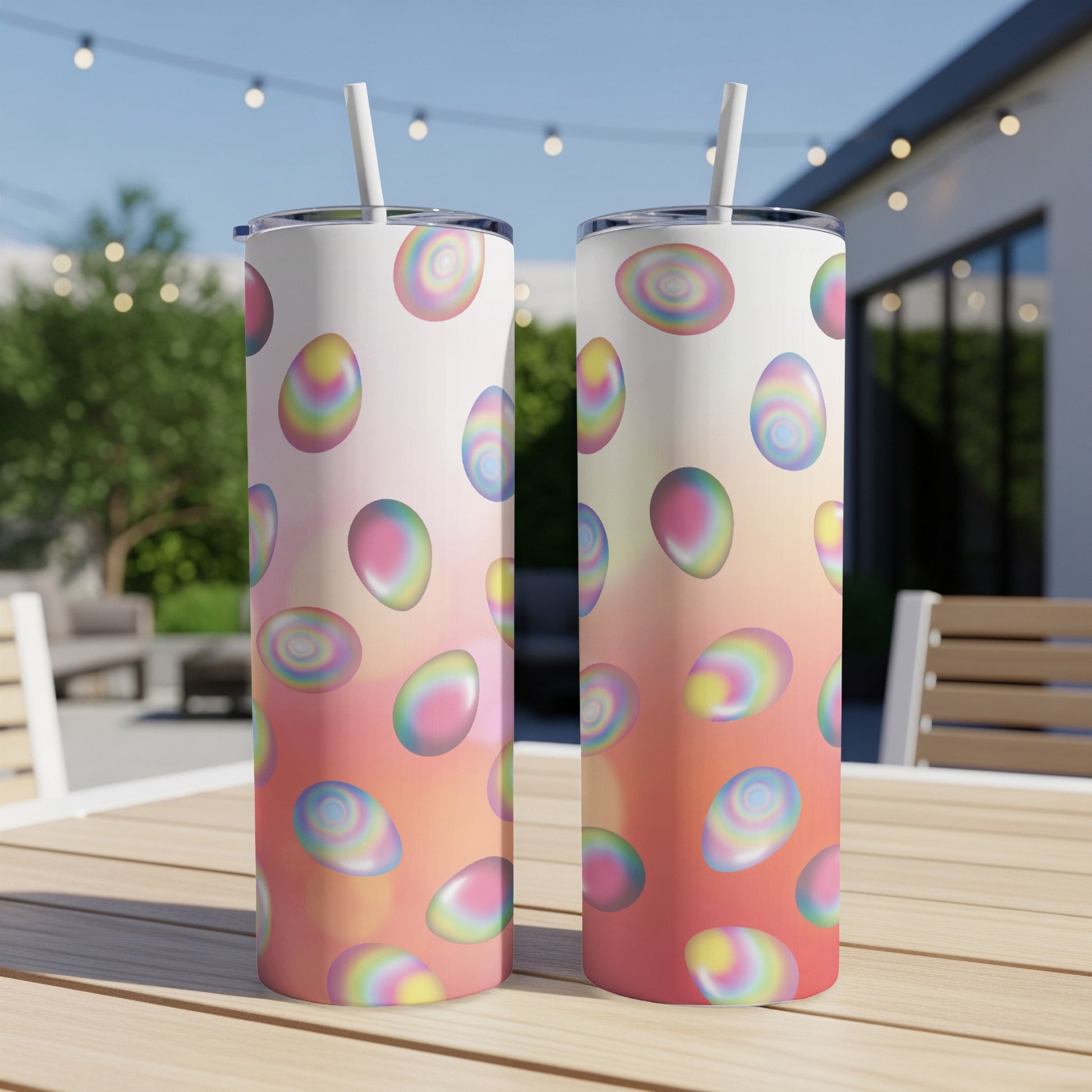 Two tall, slim tumblers with pastel egg patterns on outdoor patio table.