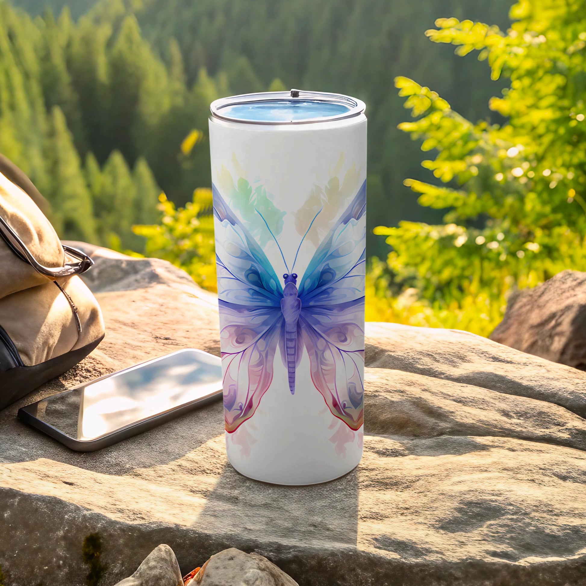 White tumbler with a watercolor butterfly design, resting on rocks.